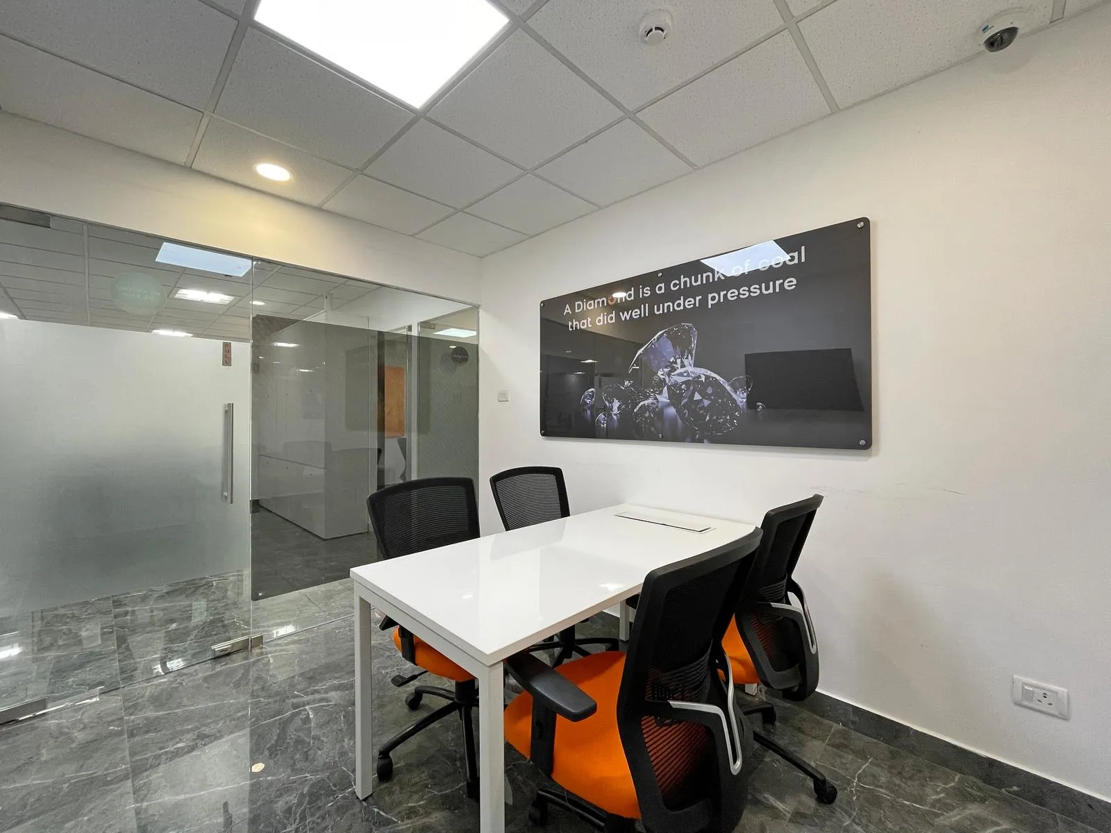 The meeting room combines a sleek, rectilinear layout with modern finishes to support focused discussions and collaboration. Polished flooring, frosted glass partitions, and ergonomic furniture create a professional, visually balanced, and functional workspace.