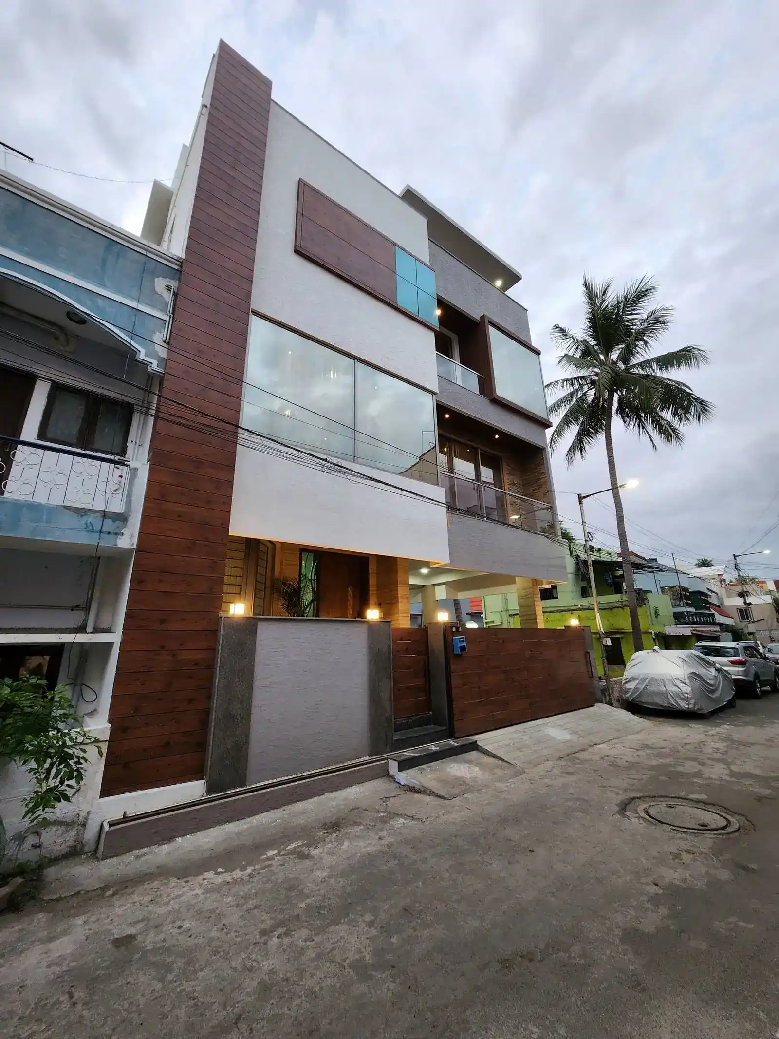 House features a multi-story facade defined by clean lines and a thoughtful mix of materials, including wood-textured panels, expansive glass surfaces, and neutral-toned plaster, creating depth, balance, and visual harmony.