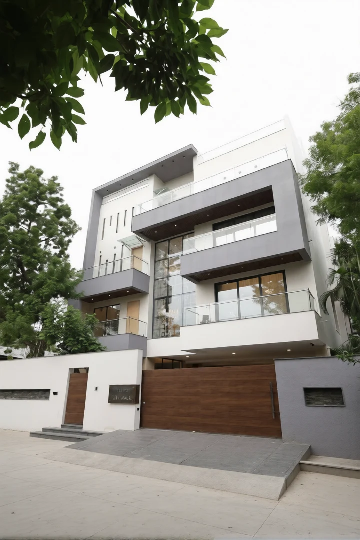 The main gate and pedestrian entry are integrated into a clean, white boundary wall, providing privacy and security.Glass railings and large windows on the upper floors add transparency and a modern touch, allowing natural light to flood the interiors.