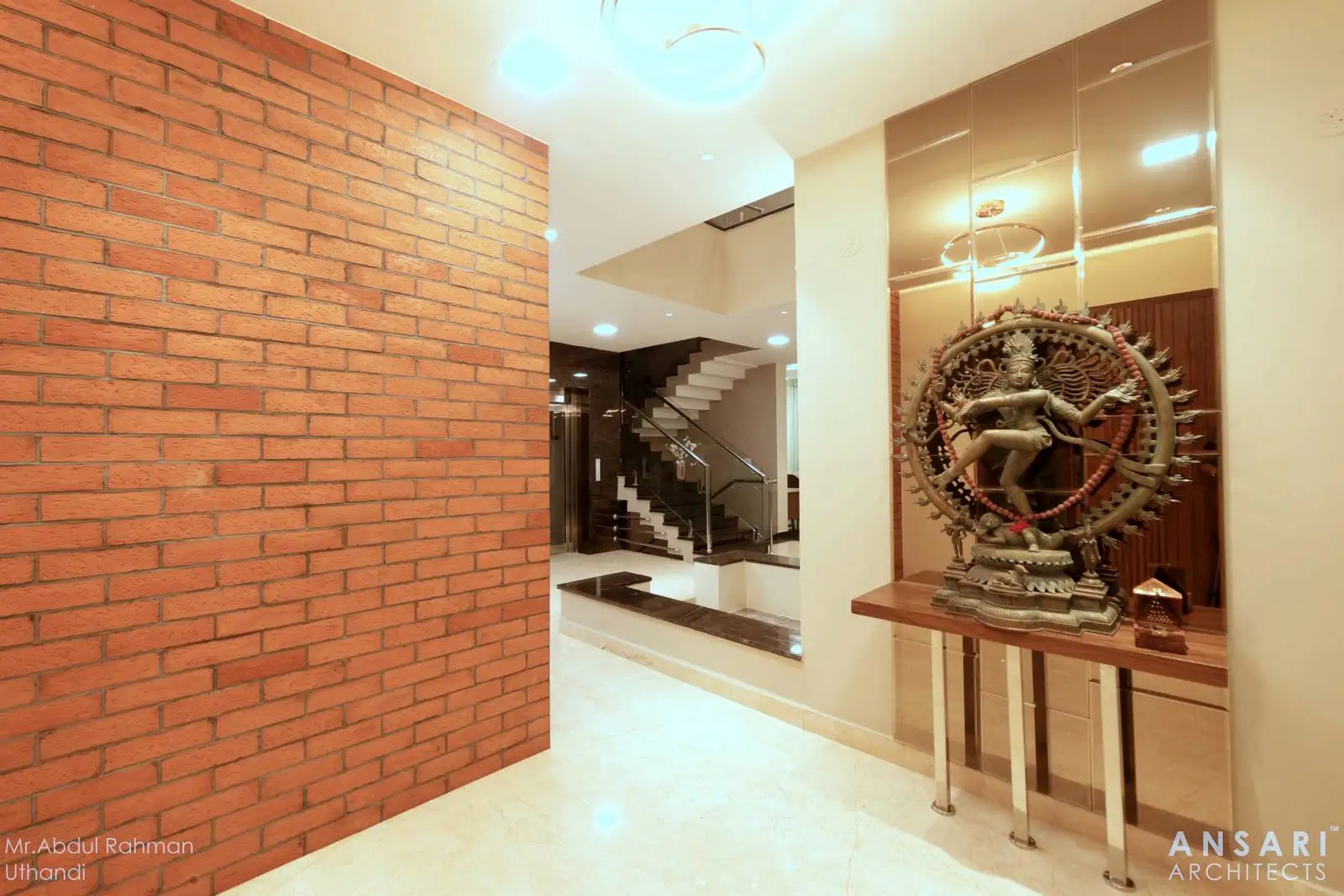 The lobby serves as a welcoming transition, featuring an exposed brick wall for warmth and character, a mirrored wall with a decorative console as a focal point, and a clear visual connection to the staircase leading to the upper floor.