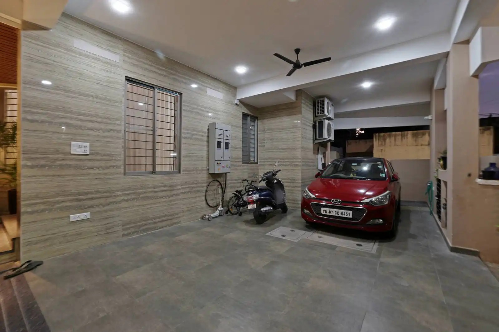 Car parking area is spacious, accommodating both a car and a two-wheeler, with additional space for bicycles or storage. Multiple recessed ceiling lights ensure the area is well-lit at night, enhancing safety and visibility.