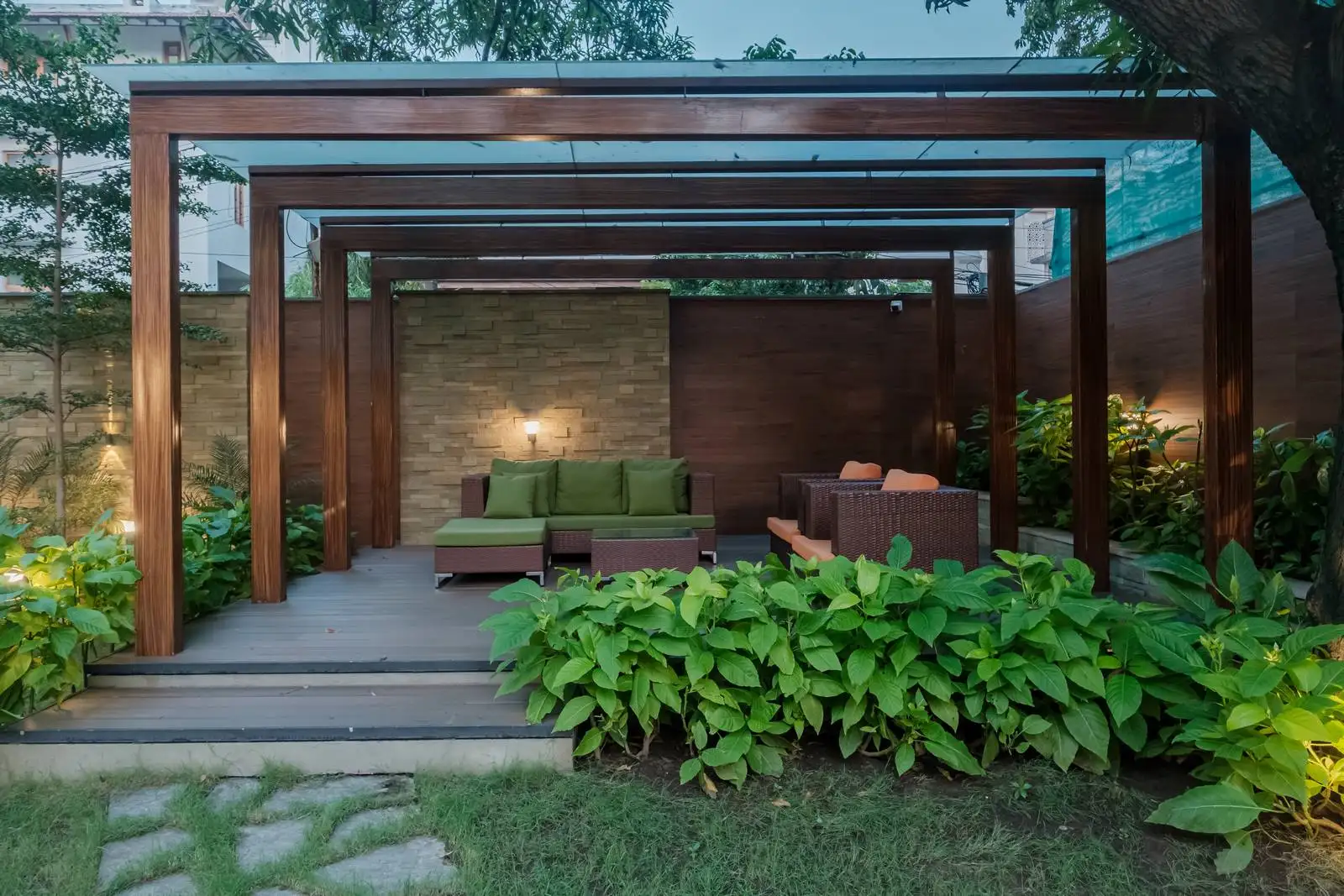 Elevated wooden pergola with modern outdoor seating, creating a cozy garden retreat framed by lush greenery and accessed via a stepped deck.