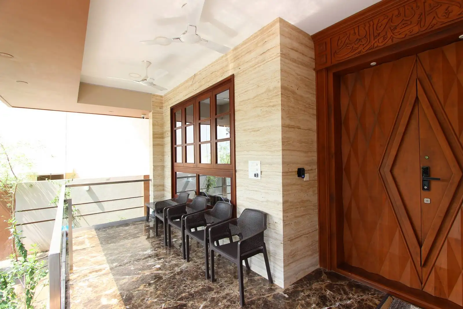 Semi-open verandah with polished marble flooring and light stone walls, featuring large wooden-framed windows and glass railings for natural light and seamless indoor-outdoor connection.