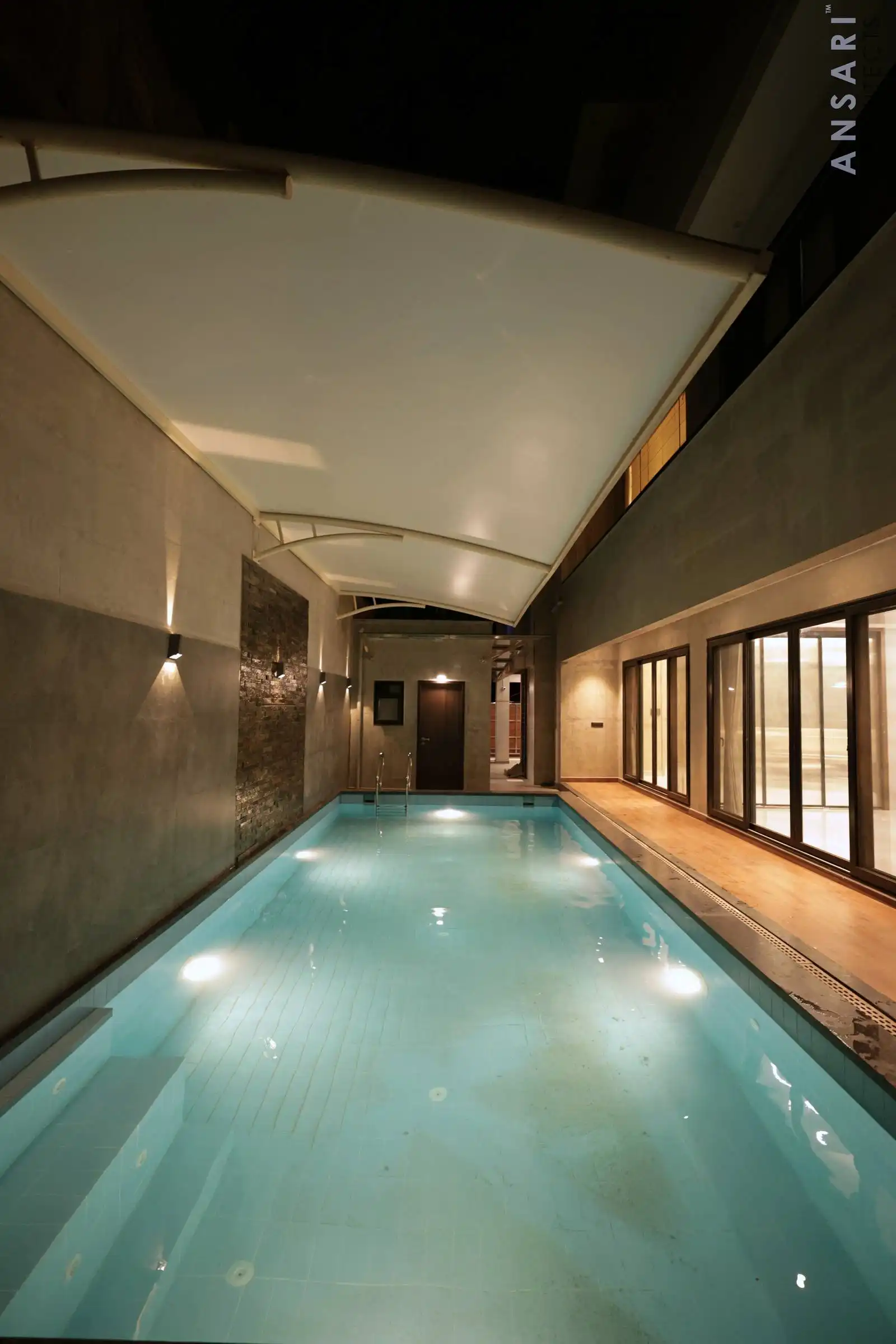 Swimming pool with tiled floor, illuminated side walls, large windows, and a curved canopy ceiling for a sleek, sheltered design.
