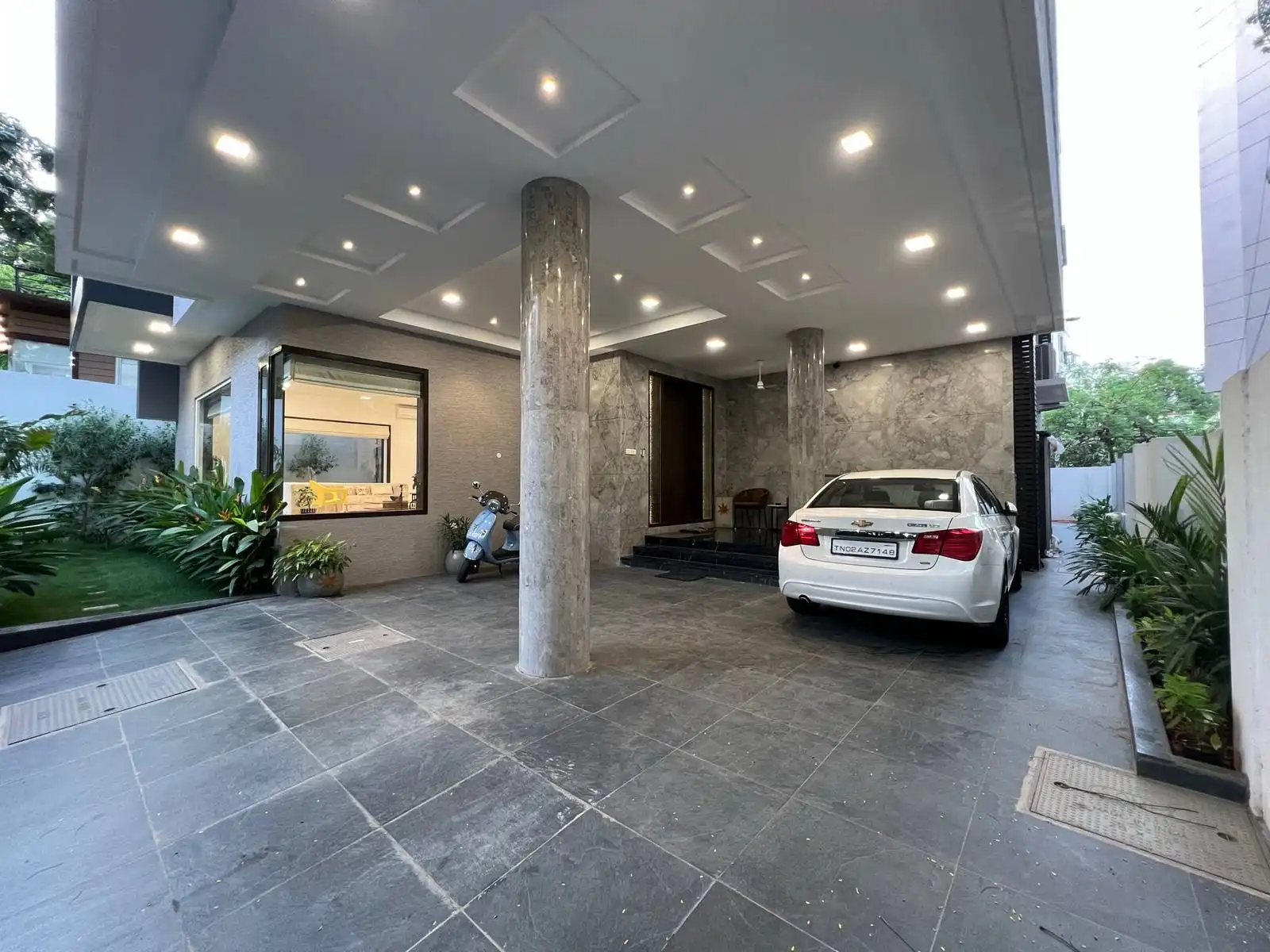 The car parking area is spacious, covered, and directly integrated with the main entrance of the house.The verandah is situated opposite the parking area, slightly elevated with steps leading up to the main entrance, creating a welcoming transition.