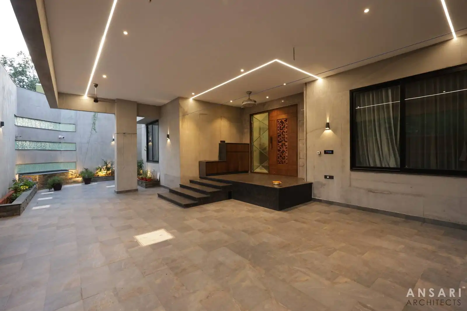 Minimalist entrance verandah with beige tiles, wooden door, and textured glass wall. Car parking enhances the functional layout.