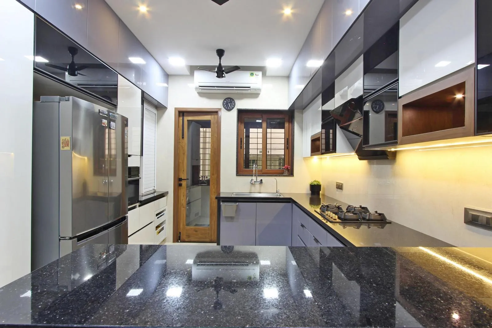 The U-shaped kitchen features black granite countertops, sleek grey and black cabinets, and integrated appliances. Its open connection to the dining area, natural light, and high ceilings create a bright, modern, and functional space.