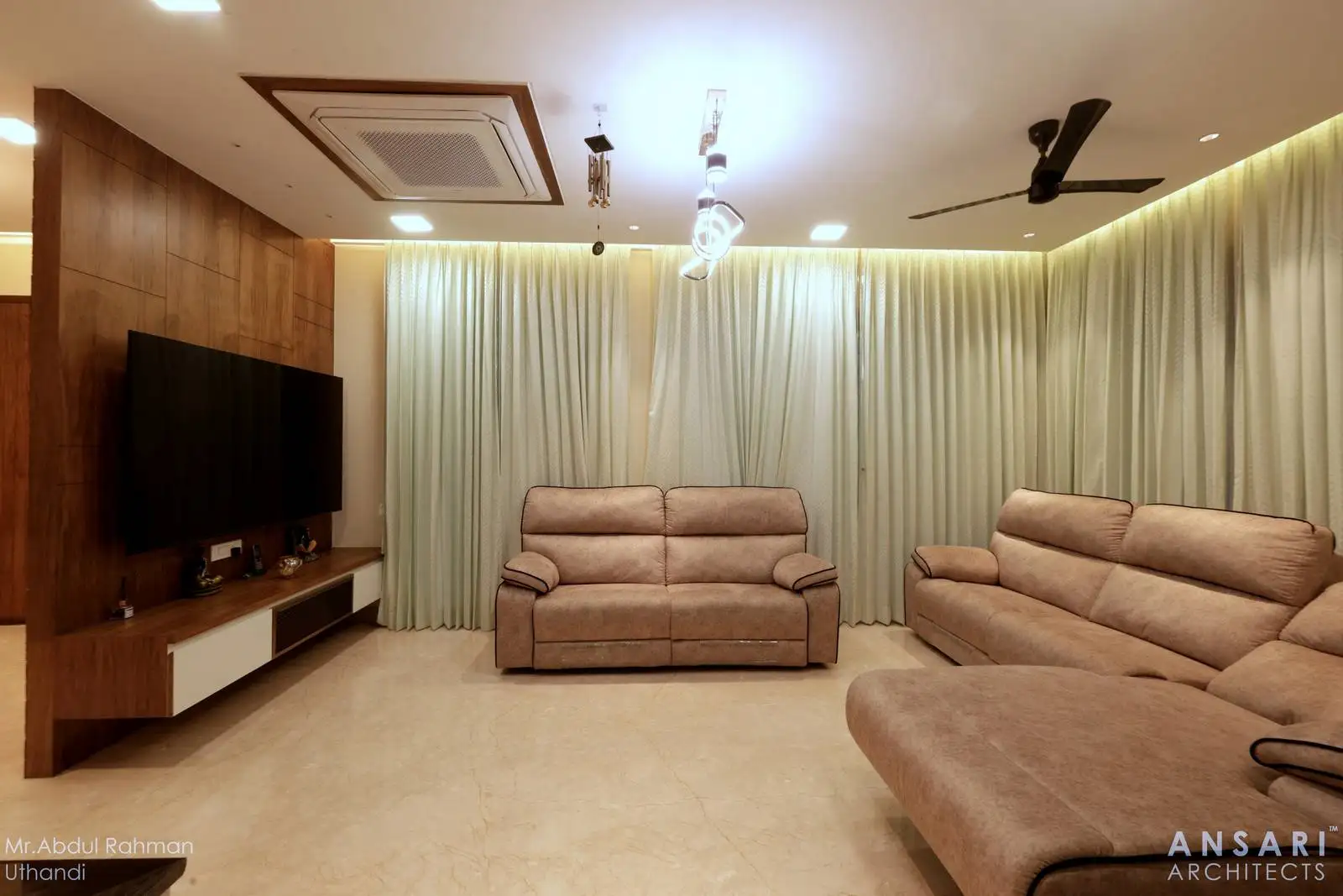 The first floor living room is designed with two large, floor-to-ceiling windows positioned at the corner, creating an L-shaped expanse of glass behind the seating area.