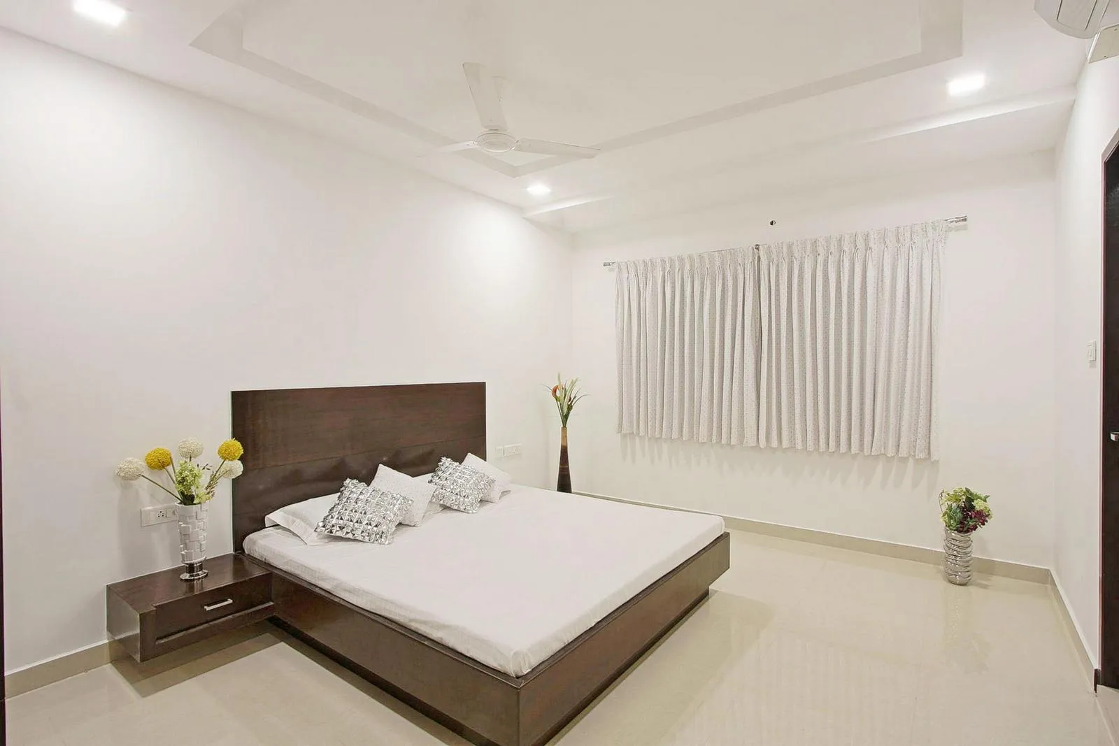 The bedroom rectilinear layout and minimal furnishings create an open, calm space, with the bed as the focal point. Integrated furniture, lighting, and subtle accents enhance comfort while keeping a clean, minimalist look.