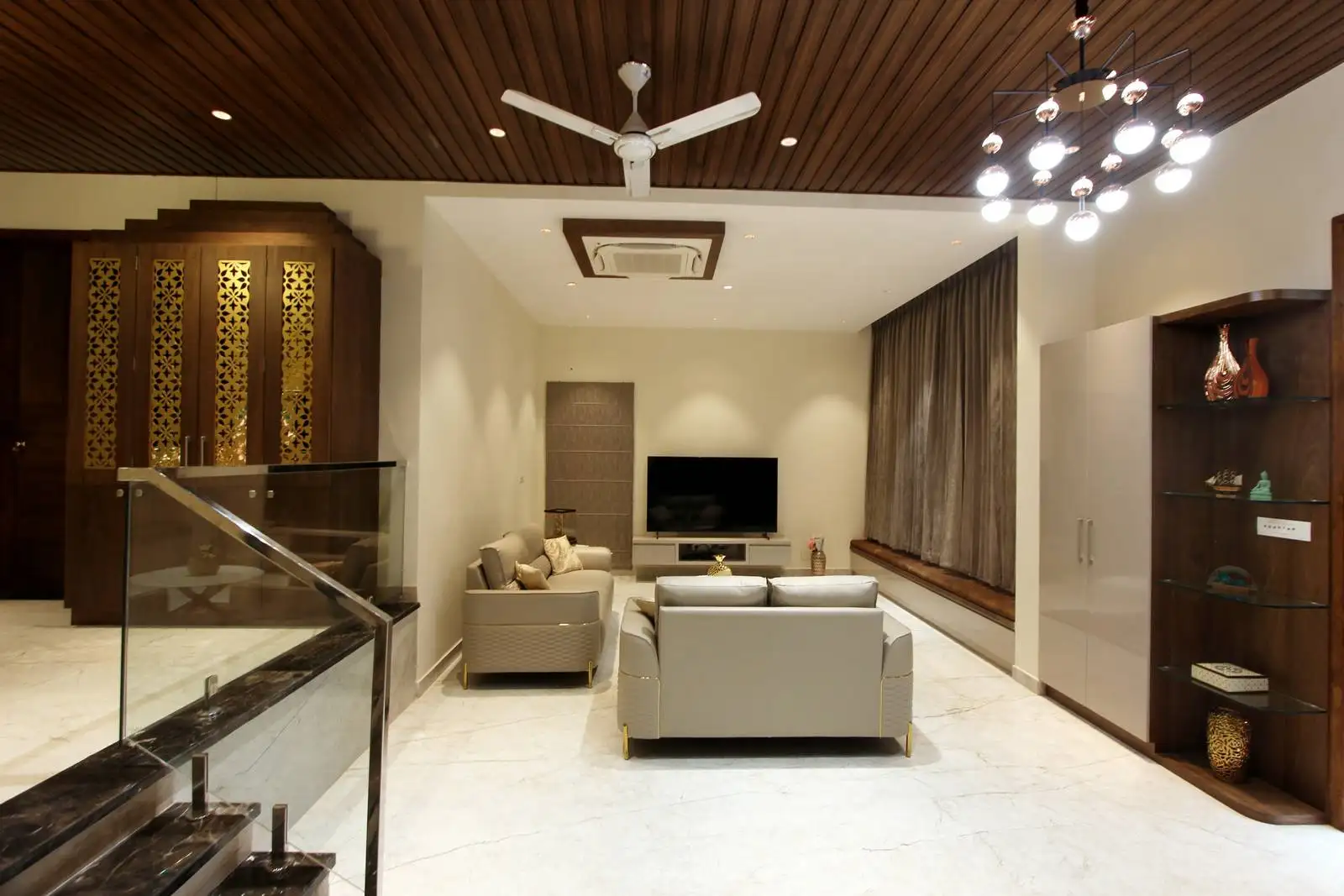 A finely crafted wooden enclosure with golden lattice doors offers privacy and a sacred ambiance, while the open-plan layout ensures seamless flow between seating, entertainment, and movement zones.