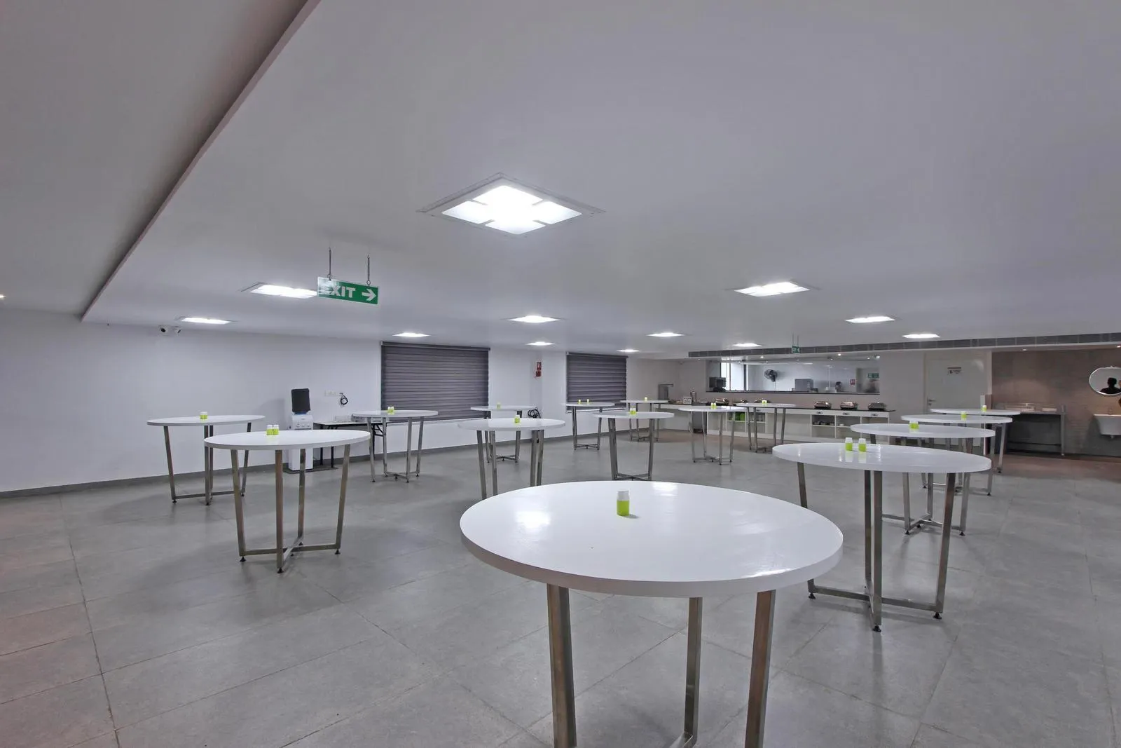 Minimalist cafeteria interior design with circular dining tables, durable vitrified tile flooring, and matte white finishes for enhanced brightness and hygiene. Recessed LED lighting, stainless steel service counters, and efficient spatial planning ensure a functional, high-traffic dining environment.