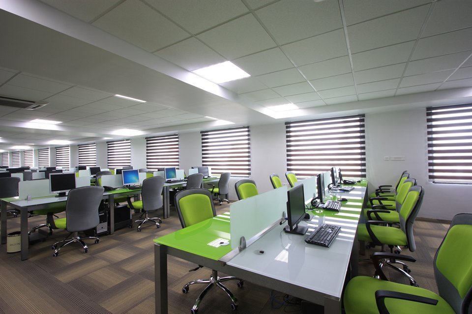The workspace features ergonomic seating, structured desks, and ample natural light. A clean layout with green accents enhances comfort, productivity, and visual appeal.