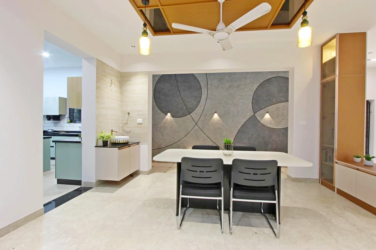 The dining area connects the kitchen and courtyard, supporting smooth movement and visual flow. Marble floors, textured accent walls, and a wooden ceiling add warmth, depth, and a modern, cohesive look.