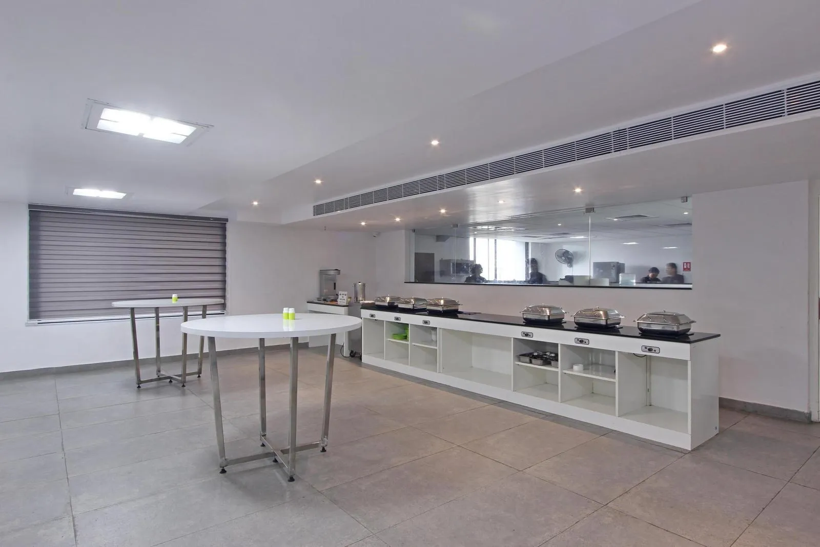 Modern cafeteria interior design featuring a linear buffet counter with granite top, stainless steel high tables, and durable vitrified tile flooring. Matte white finishes,