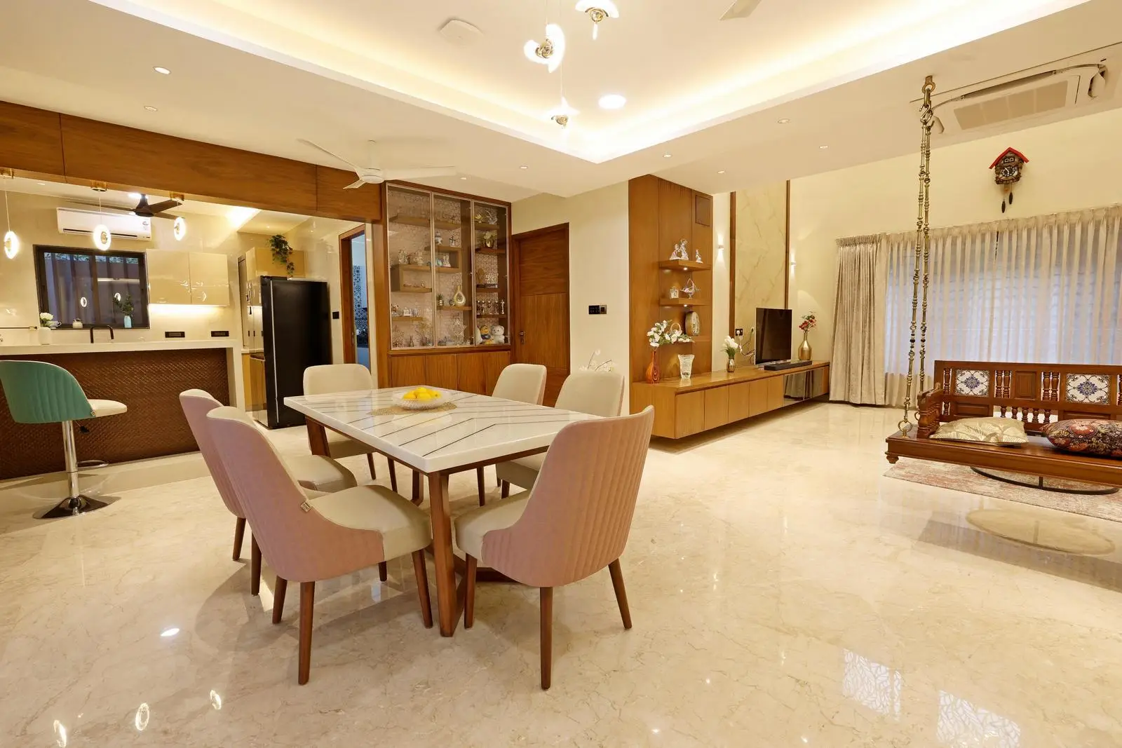 The centrally placed dining table links living, kitchen, and circulation zones, while the staircase adds vertical depth. Polished marble floors, wooden ceilings, and cream walls create a warm, bright, and cohesive palette. 