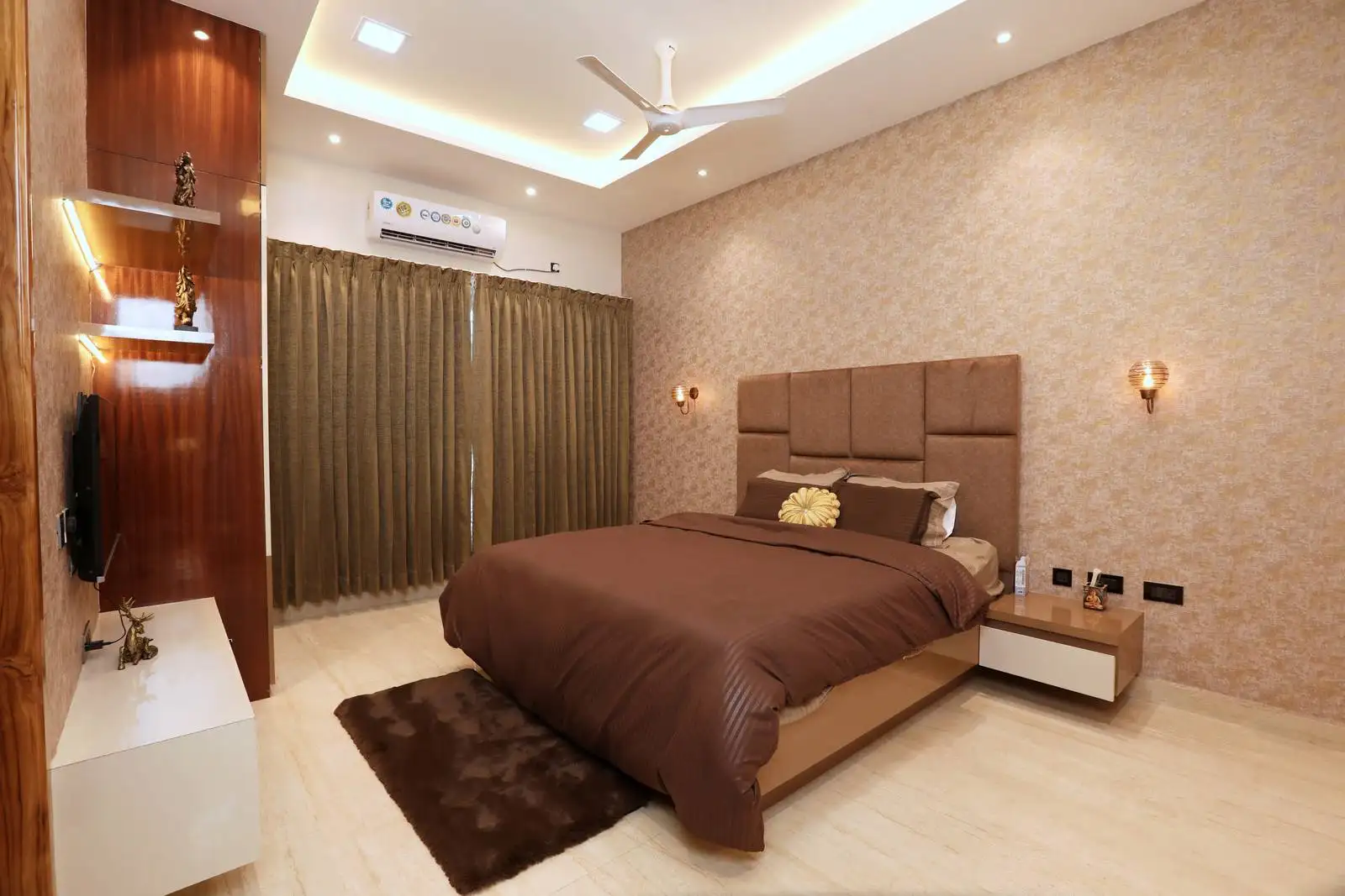 The bedroom is spacious and thoughtfully arranged with the bed as the focal point. A subtle patterned accent wall adds texture, while the layout allows easy movement and balanced symmetry with side tables.