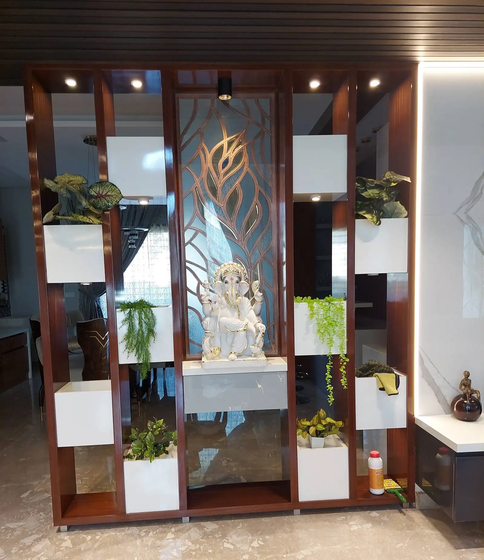 The Puja room features a decorative wooden shelving unit that serves as a custom-built altar. Warm wood tones create a sacred and traditional ambiance.