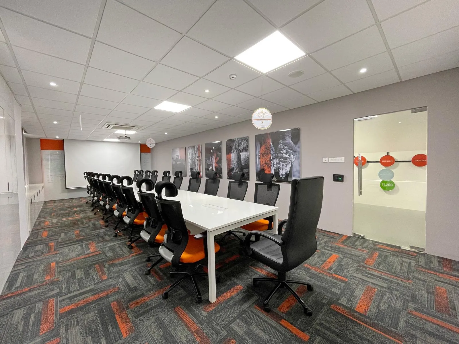 The boardroom features a 20-seater laminated conference table with ergonomic chairs and geometric carpet flooring, combining comfort, functionality, and visual rhythm. Acoustic ceilings, integrated lighting, and multimedia setups create a professional, modern, and technology-ready boardroom environment.