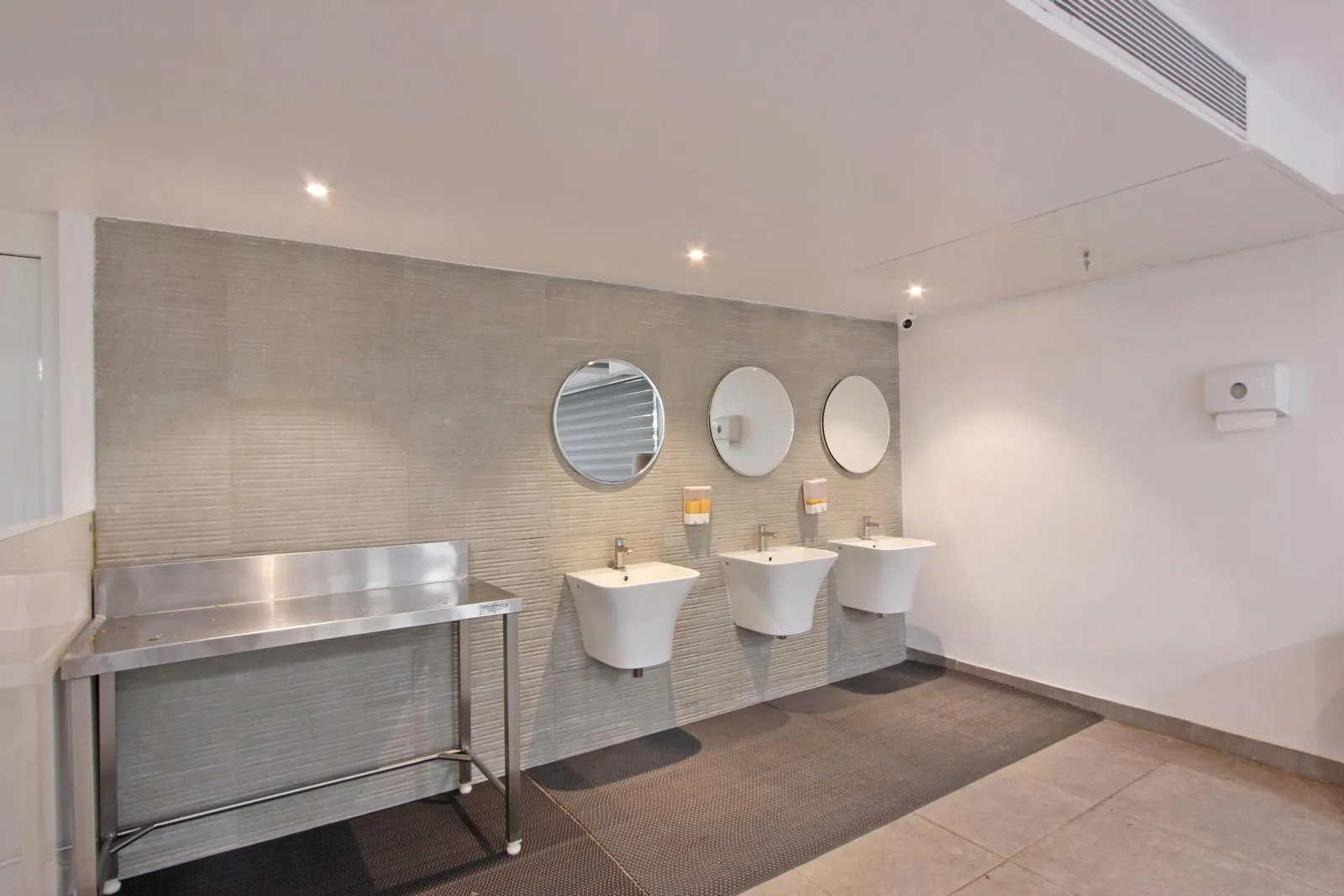 Washroom interior design featuring wall-mounted ceramic basins, round mirrors, and stainless steel fixtures for a clean, functional layout.