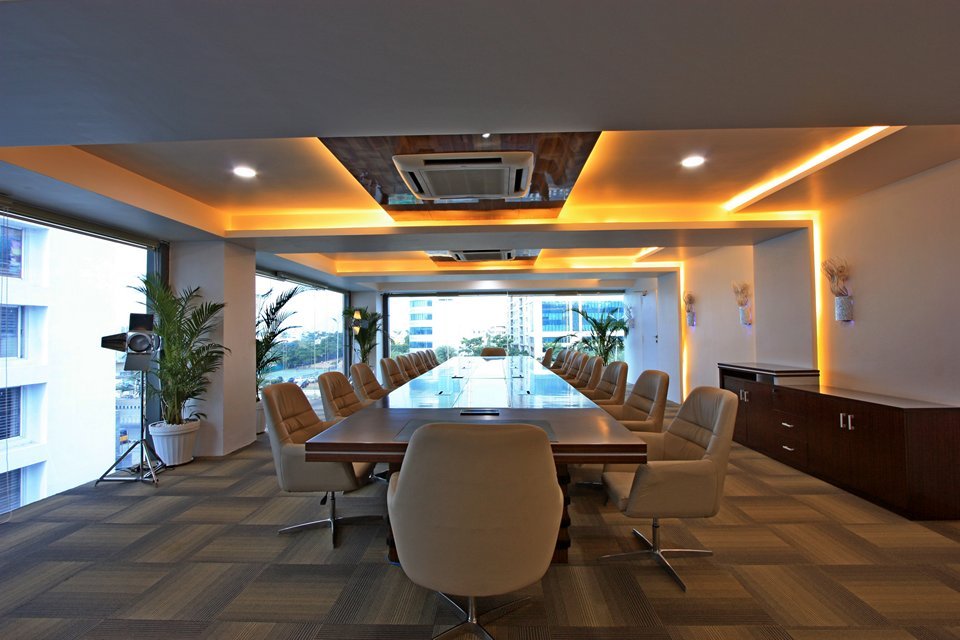 Conference room featuring a long wooden table, large windows for natural light, warm recessed lighting, potted plants, and sleek wooden cabinetry.