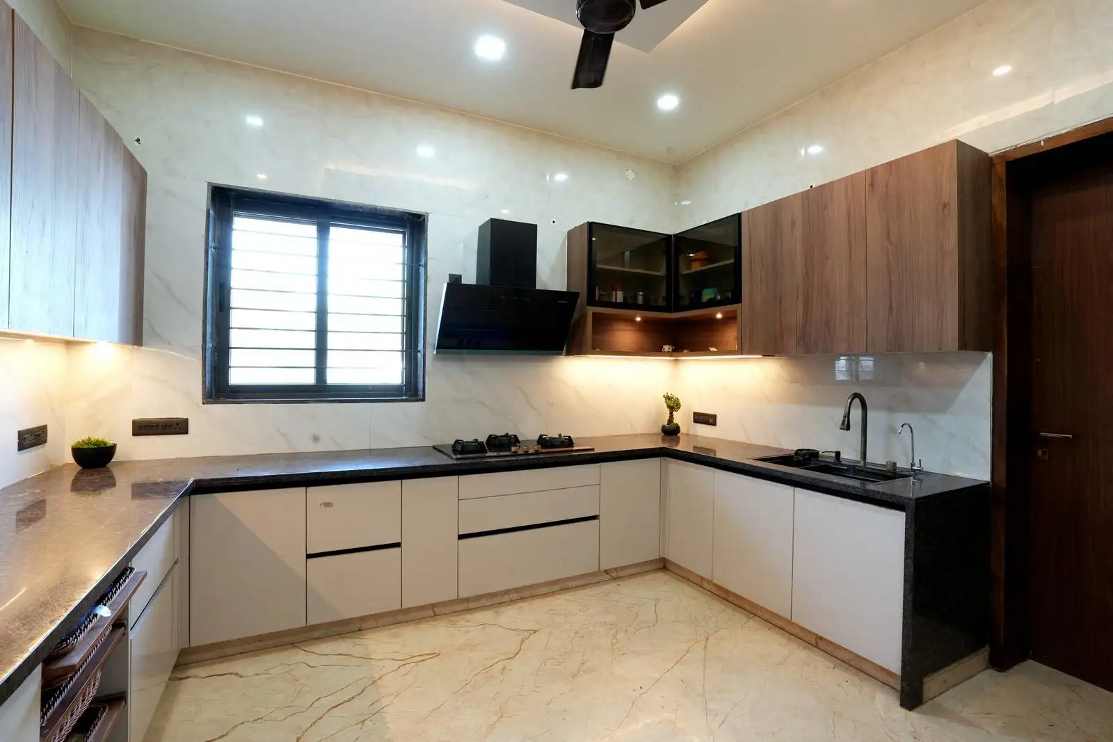 This kitchen showcases handle-less wood and matte cabinetry, seamlessly integrating appliances and task lighting. The black granite countertop adds durability and style to the space.

