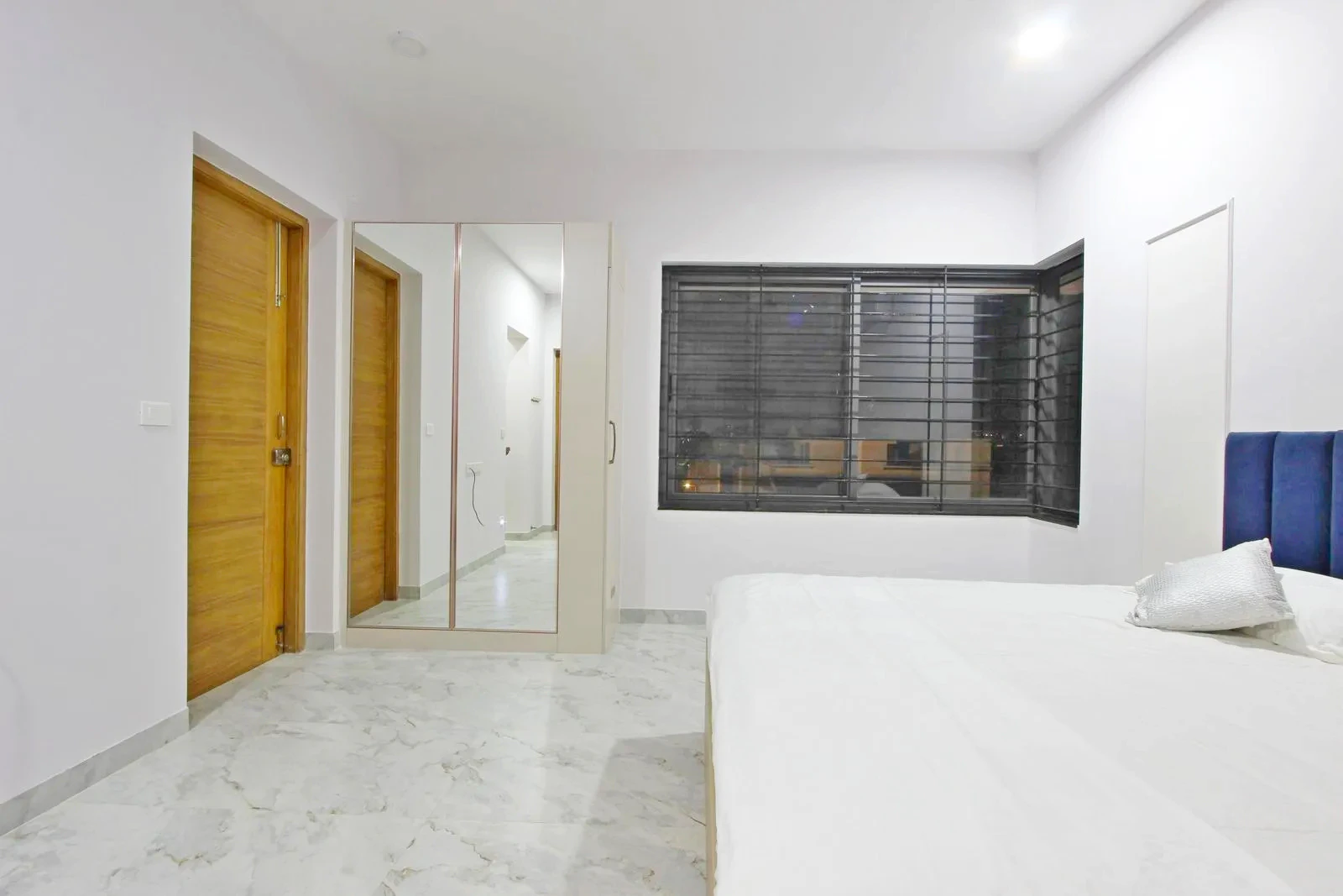 The bedroom features a linear layout with the bed oriented toward the window for natural light. Mirrored wardrobes and strategically placed doors enhance space, light, and functional zoning.