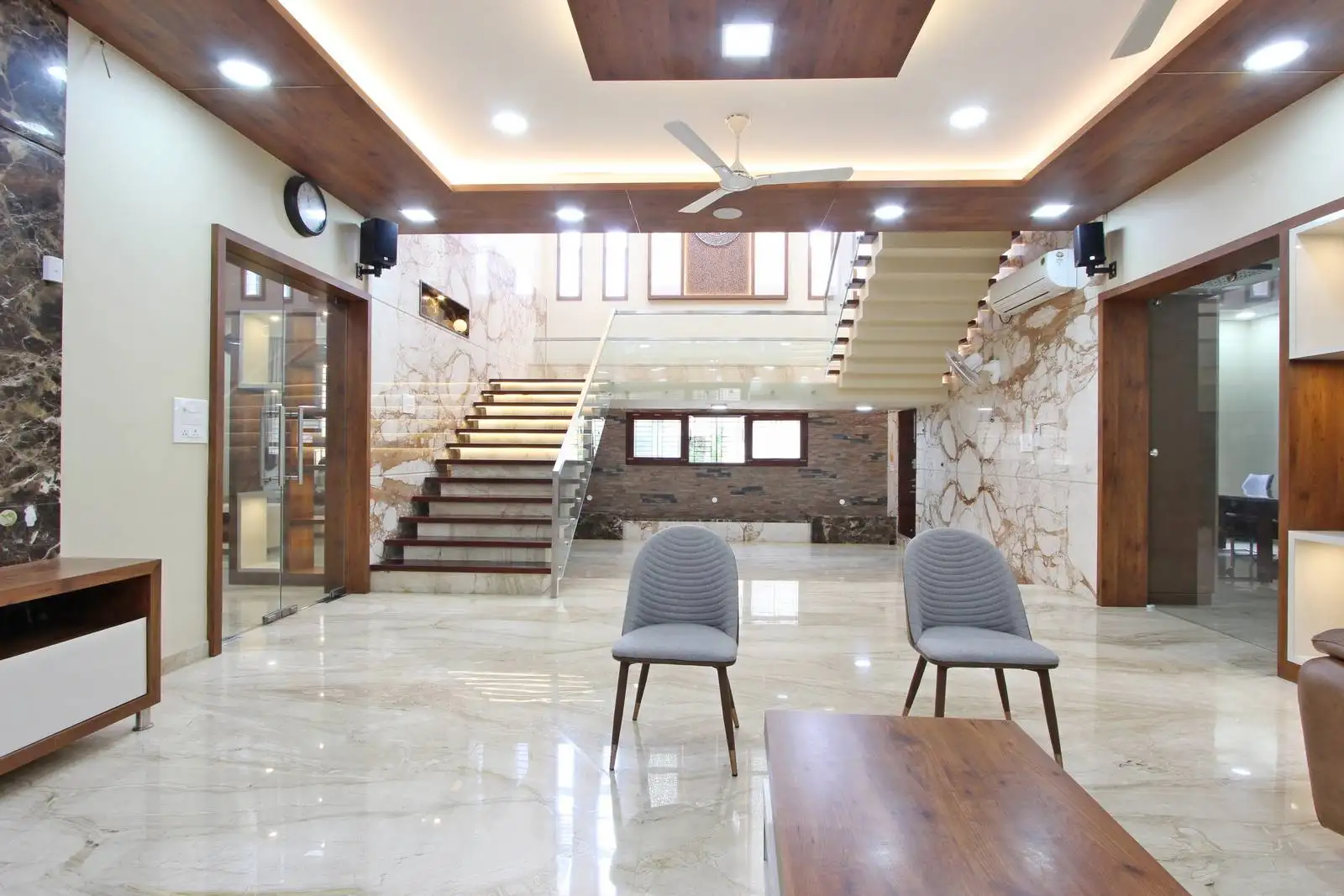 Spacious double-height living area with an open-plan layout, centered around a floating glass-railed staircase that enhances light flow and visual connectivity between levels.