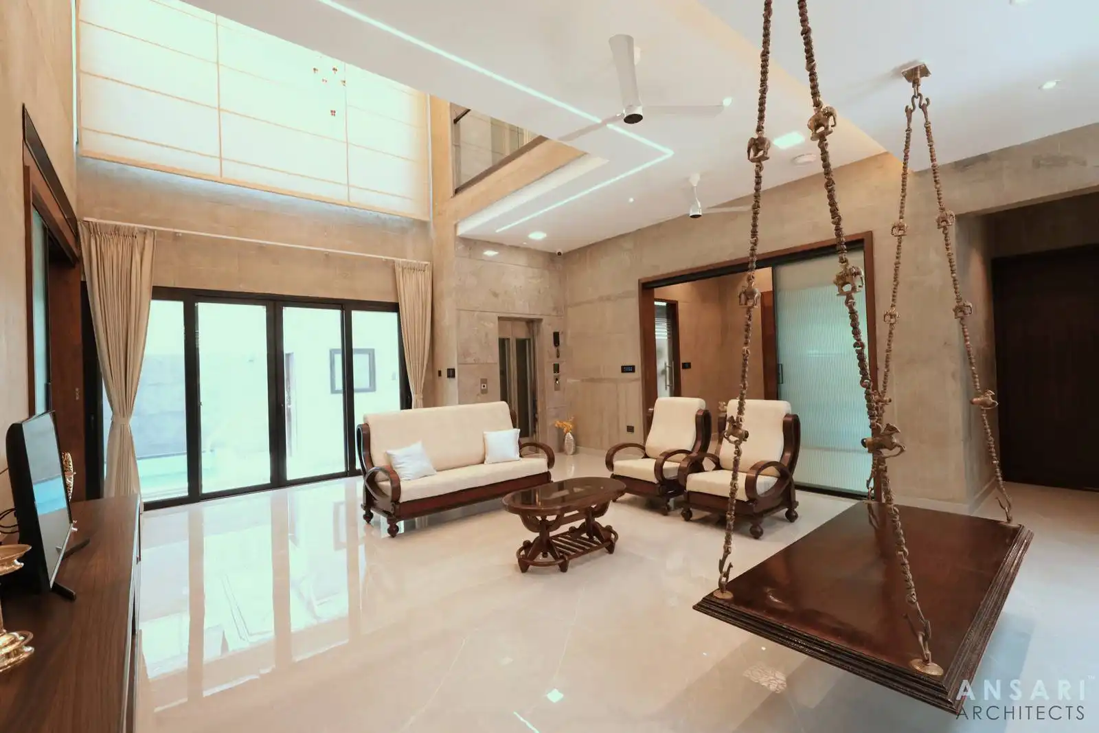 Living room with beige walls, glossy floor, suspended wooden swing, and large glass doors, emphasizing spaciousness and natural light.