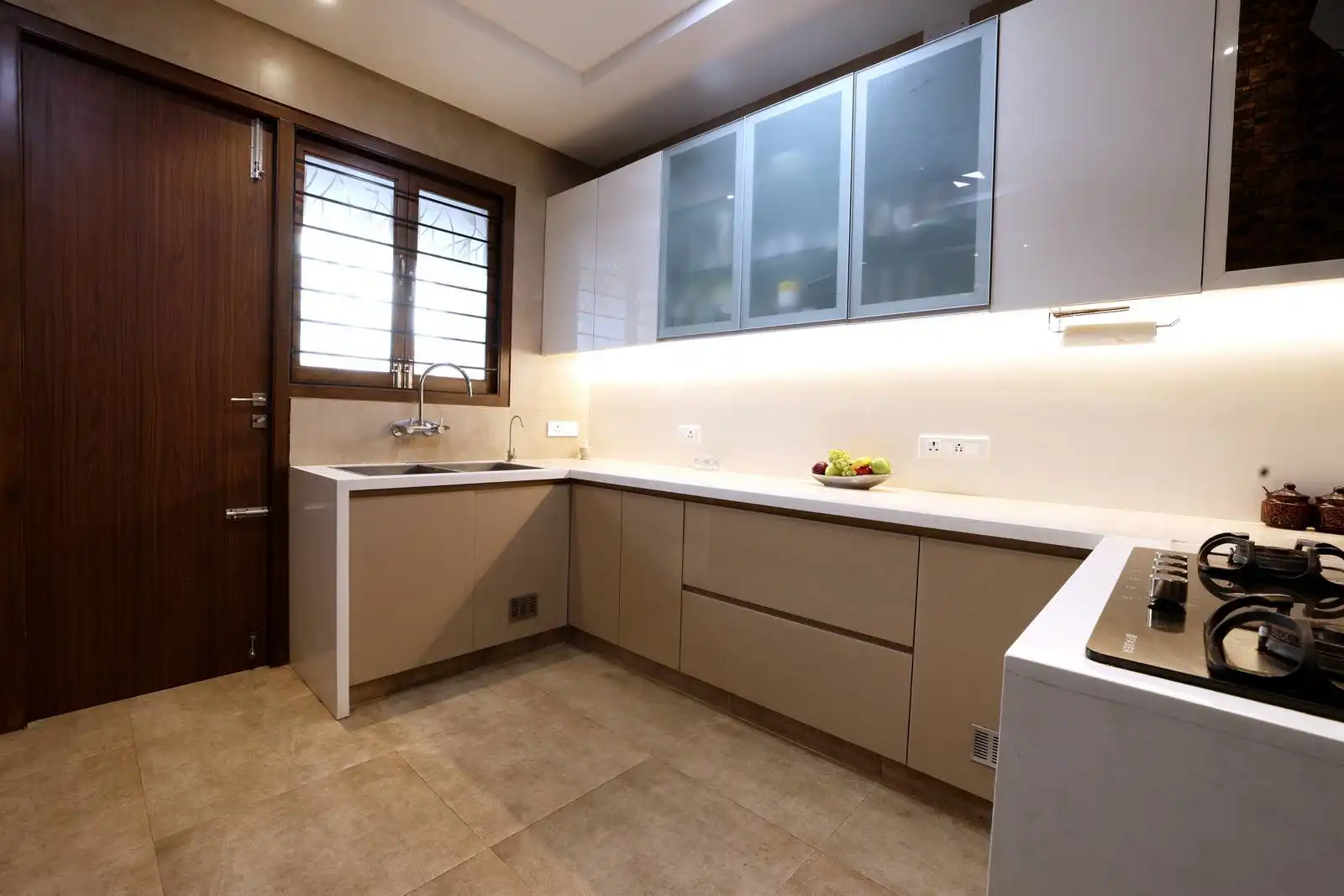 A light-toned kitchen with beige and white cabinetry, under-cabinet lighting, a window for natural ventilation, and a layout that balances efficiency and clarity.