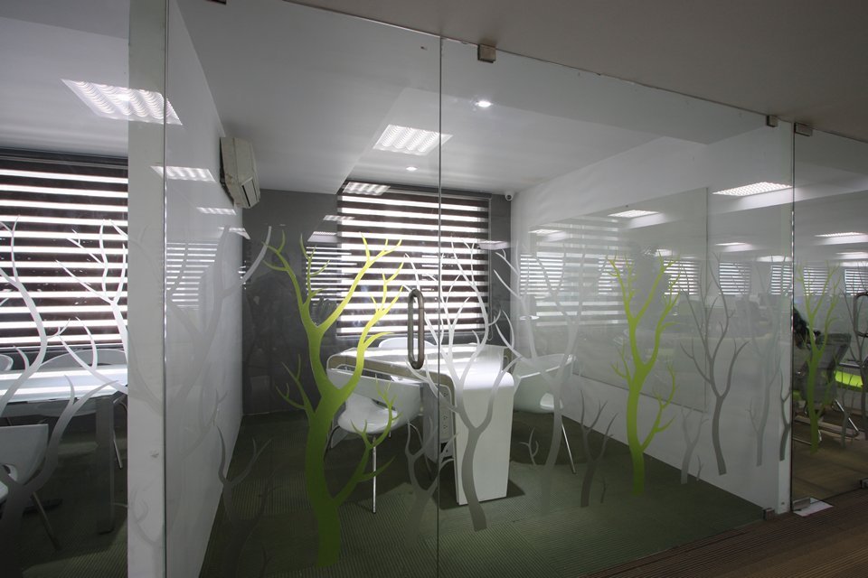 Designed small meeting room featuring glass walls with frosted tree patterns, a sleek white table, and window blinds