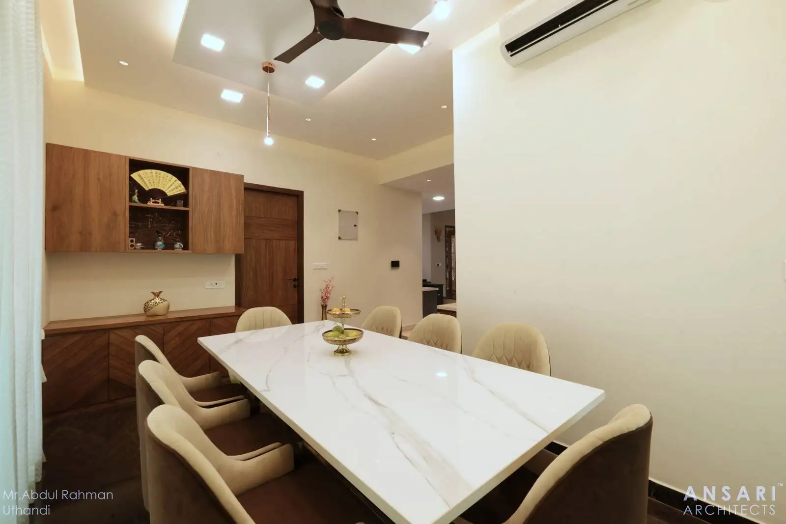 A dining space designed for both form and function, featuring a white marble table with eight upholstered chairs, integrated wooden cabinetry, and thoughtfully placed lighting and climate controls, all set against a clean, light-toned backdrop to enhance openness and elegance.