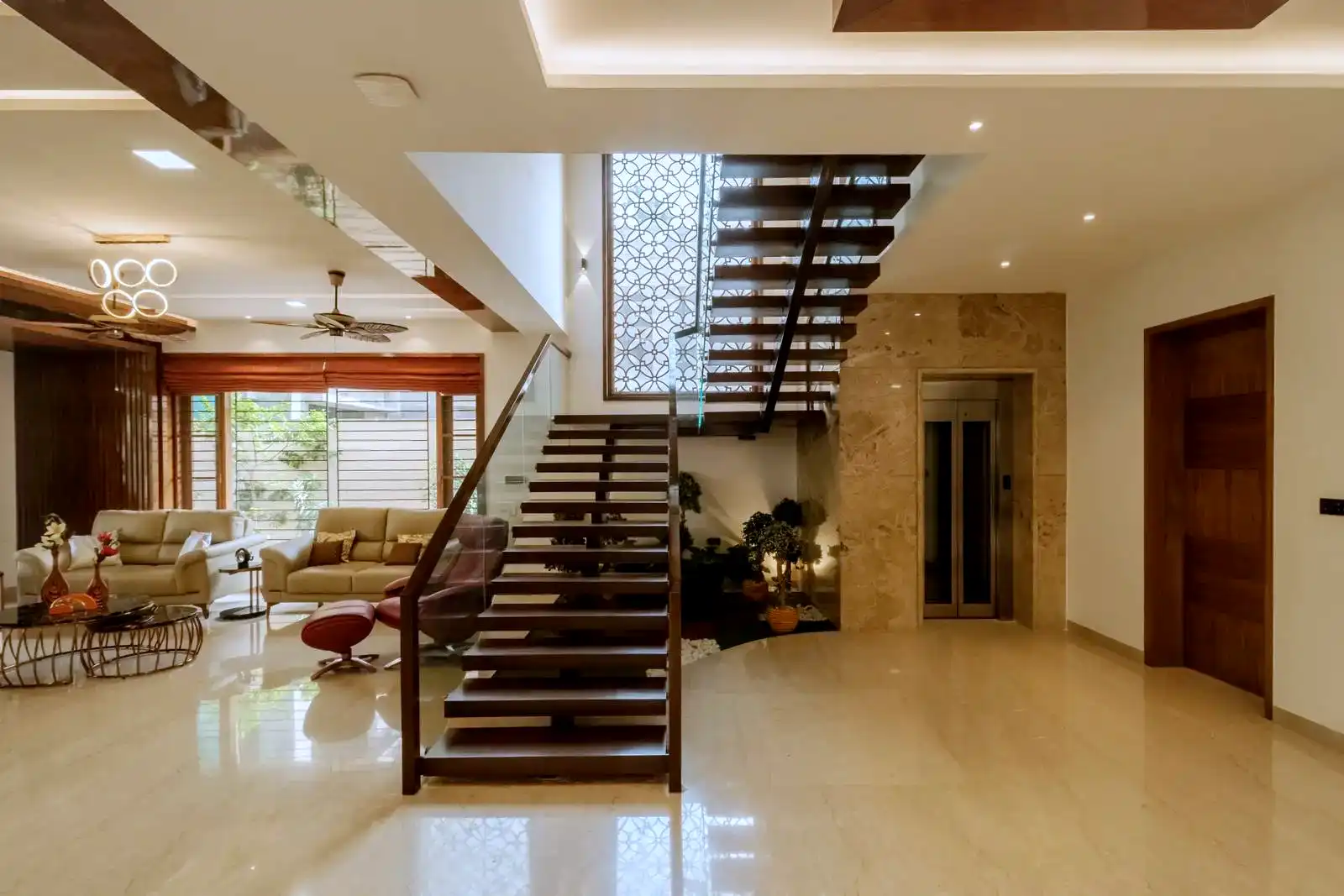 Central floating glass staircase complemented by beige tile flooring and a marble-clad elevator wall.
