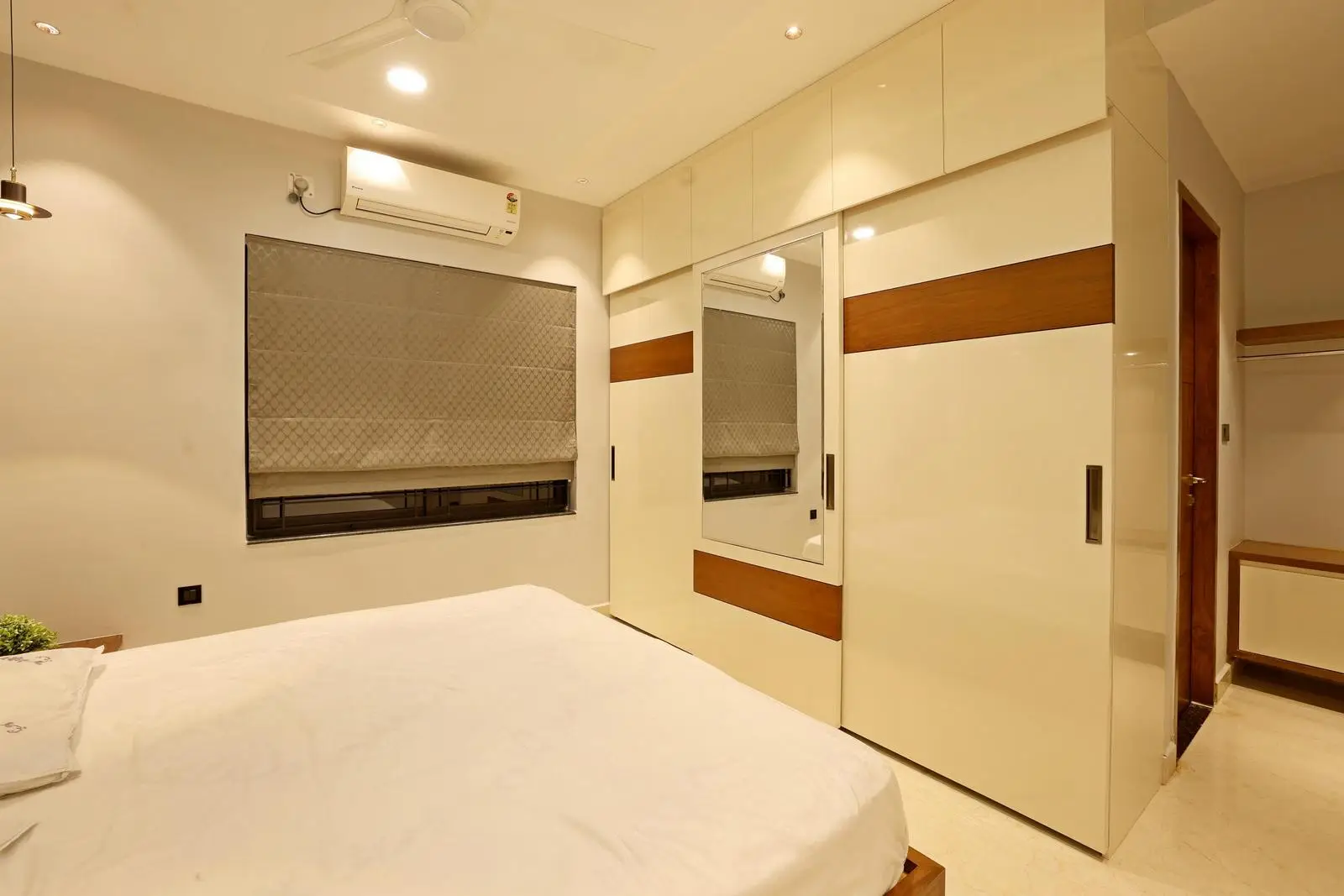 A stylish wardrobe wall and optimized circulation define the guest bedroom. Warm beige and wood tones create a calm, inviting palette, while handle-less storage and recessed lighting ensure a sleek, minimalist design.