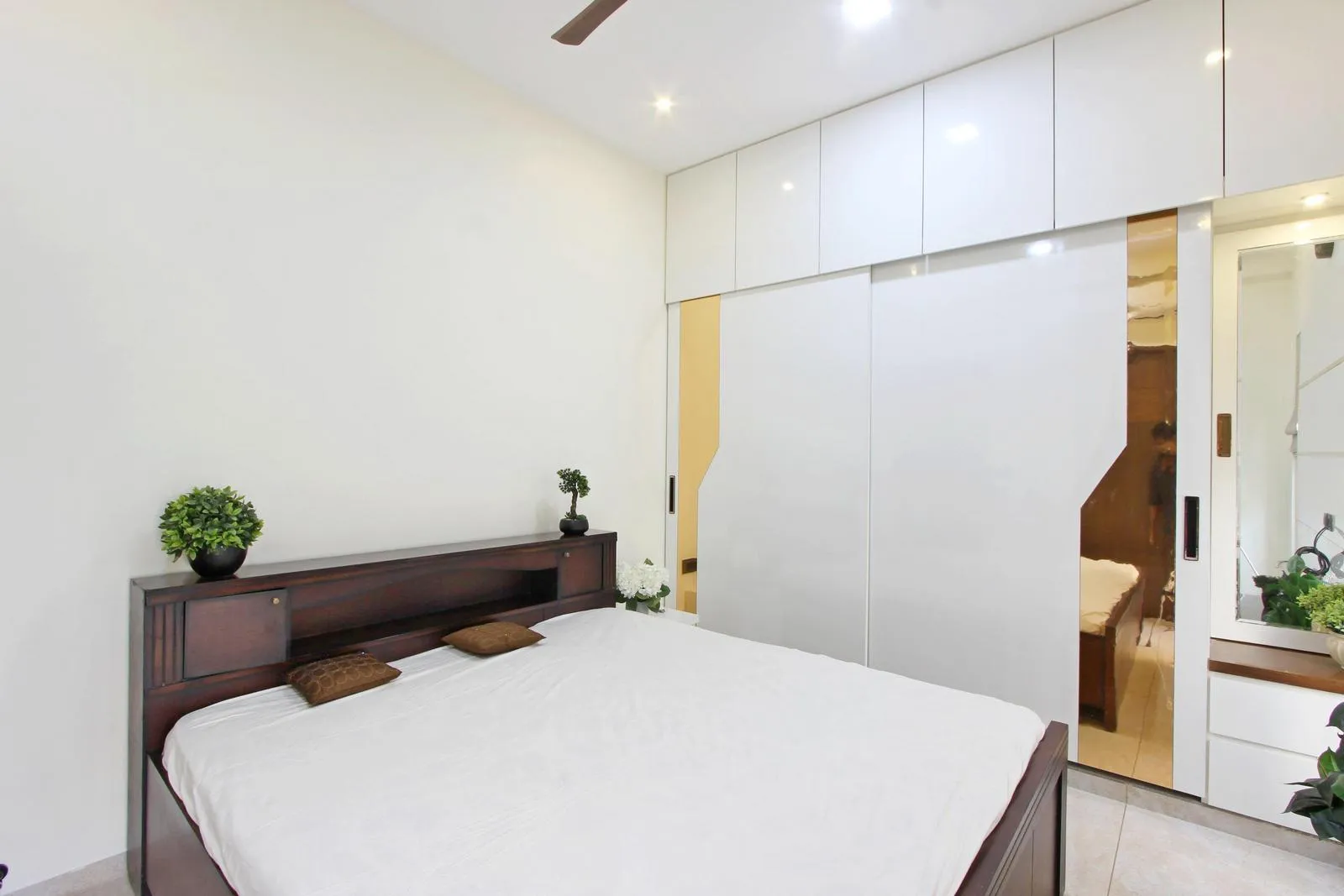 This compact bedroom 3 is smartly planned with a central bed, sliding wardrobe, and integrated dresser for efficient use of space. Light neutral tones, reflective finishes, mirrors, modern feel while improving circulation and visual openness.