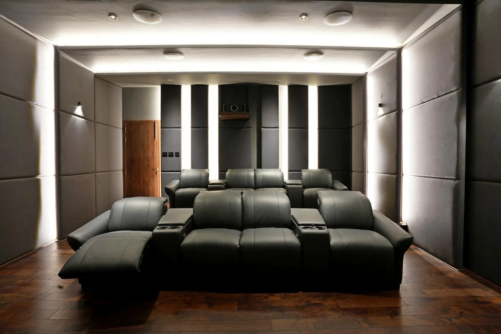 Acoustic fabric wall panels, dark wooden flooring, and black leather recliners create a refined, immersive viewing environment. Integrated lighting, concealed speakers, and tiered seating ensure optimal sound quality, comfort, and visual focus.
