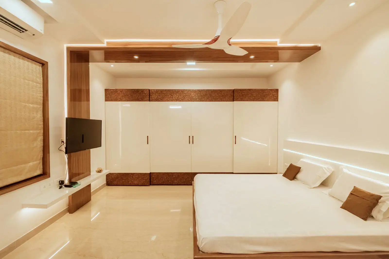 Glossy white wardrobe with wooden accents offers sleek, ample storage, while the wooden ceiling panel with LED strip lighting adds warmth and contemporary style.