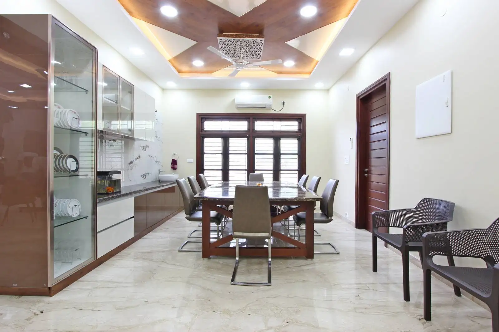 Spacious dining area with a six-seat glass-top table, elegant marble flooring, custom cabinetry, and a striking ceiling design featuring cove lighting and a modern chandelier.