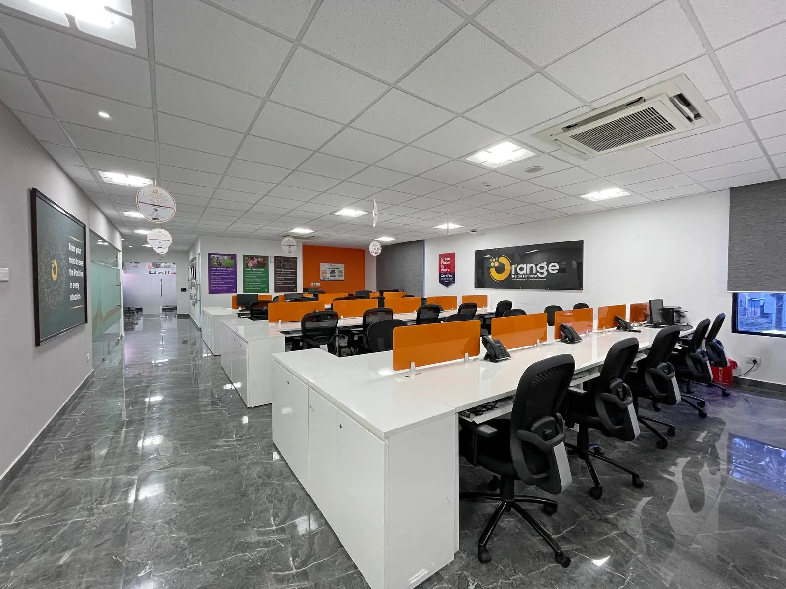 This 30-seater open-plan workstation area combines white laminate desks, orange divider panels, and ergonomic seating to create a collaborative, high-efficiency workspace. Grey marble flooring, acoustic ceilings, and glass partitions enhance light, comfort, and a dynamic corporate aesthetic.