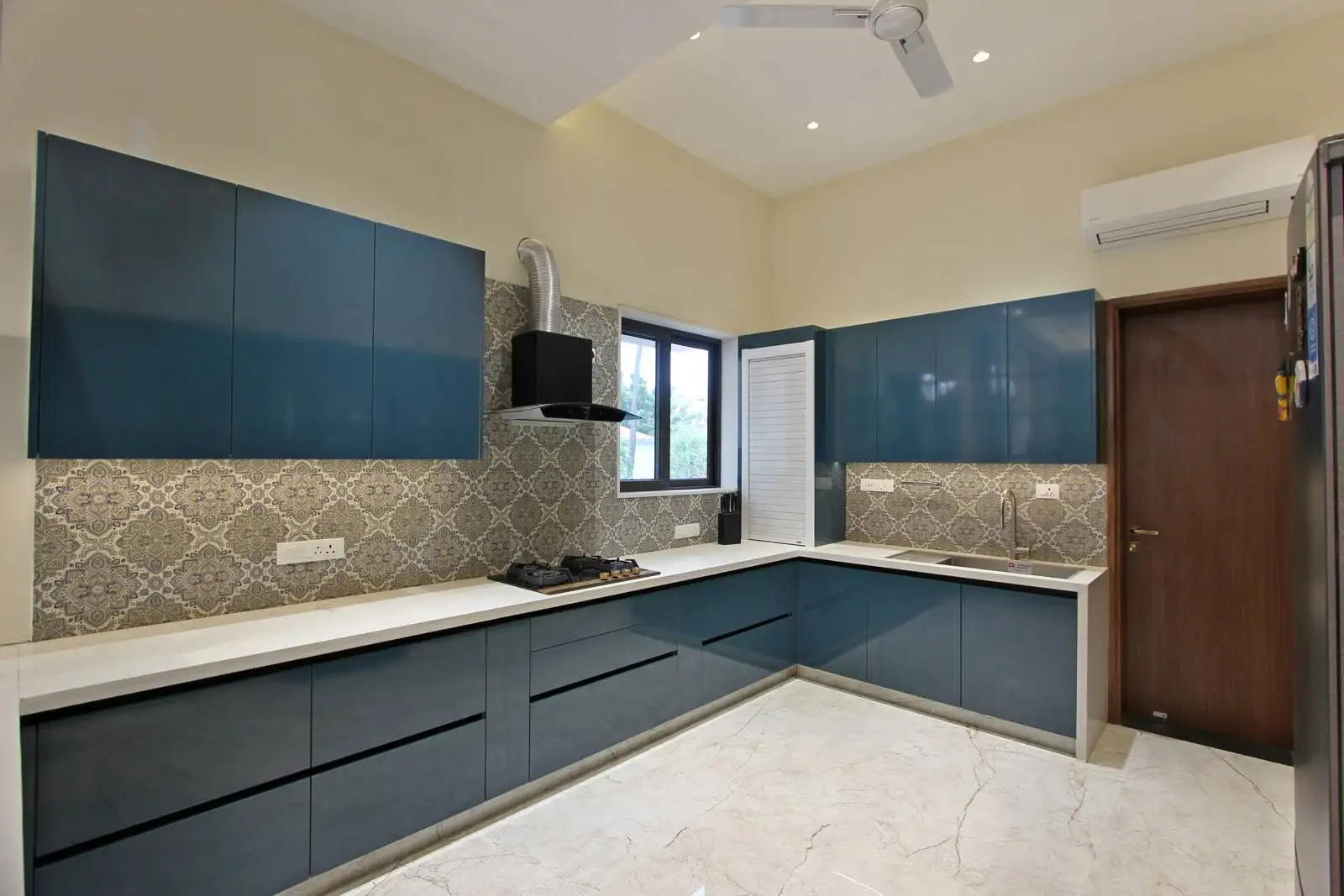 Sleek handle-less blue cabinets paired with white countertops create a bold, modern kitchen. Patterned backsplash and light flooring add contrast and visual texture.