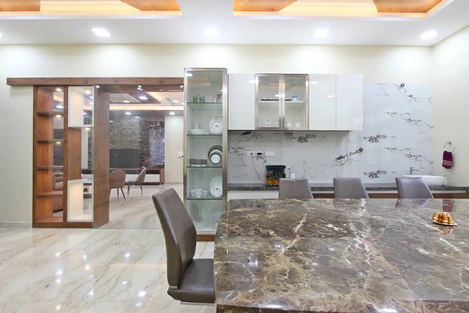 Open dining area with a central marble-top table, upholstered chairs, and polished marble flooring, seamlessly connected to the living space for a refined and functional layout.