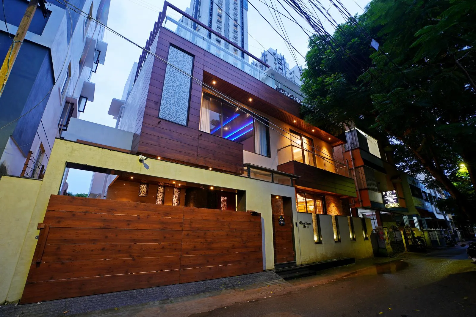 A house with wooden exterior elements and large glass windows glows warmly at dusk. Clean lines, layered facades, and subtle lighting reflect a refined, contemporary architectural design.