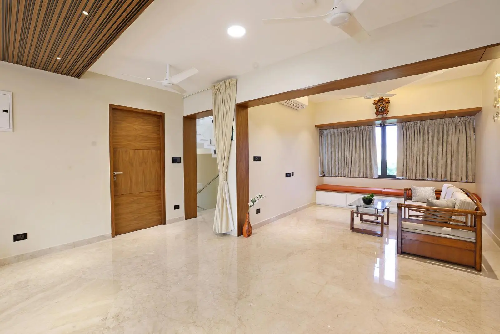 The first-floor family lounge and study area use an open-plan layout with seating by the window. Beige marble floors, cream walls, and wooden accents create a warm, balanced palette. Recessed lighting, built-in seating, and a curtain partition add functionality and elegance.