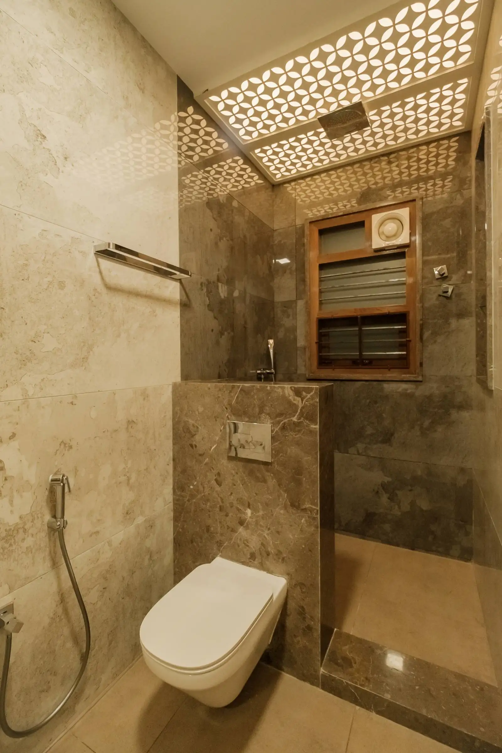 Marble-finished bathroom with rainfall shower, wall-mounted toilet, and decorative ceiling lighting for a stylish, airy feel.