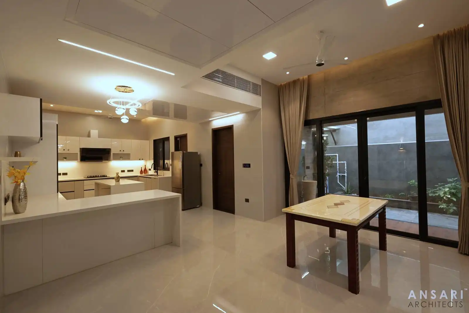 Open kitchen and dining area with sleek cabinetry, layered lighting, and glass doors blending indoor-outdoor flow, enriched by warm wood accents and polished finishes.