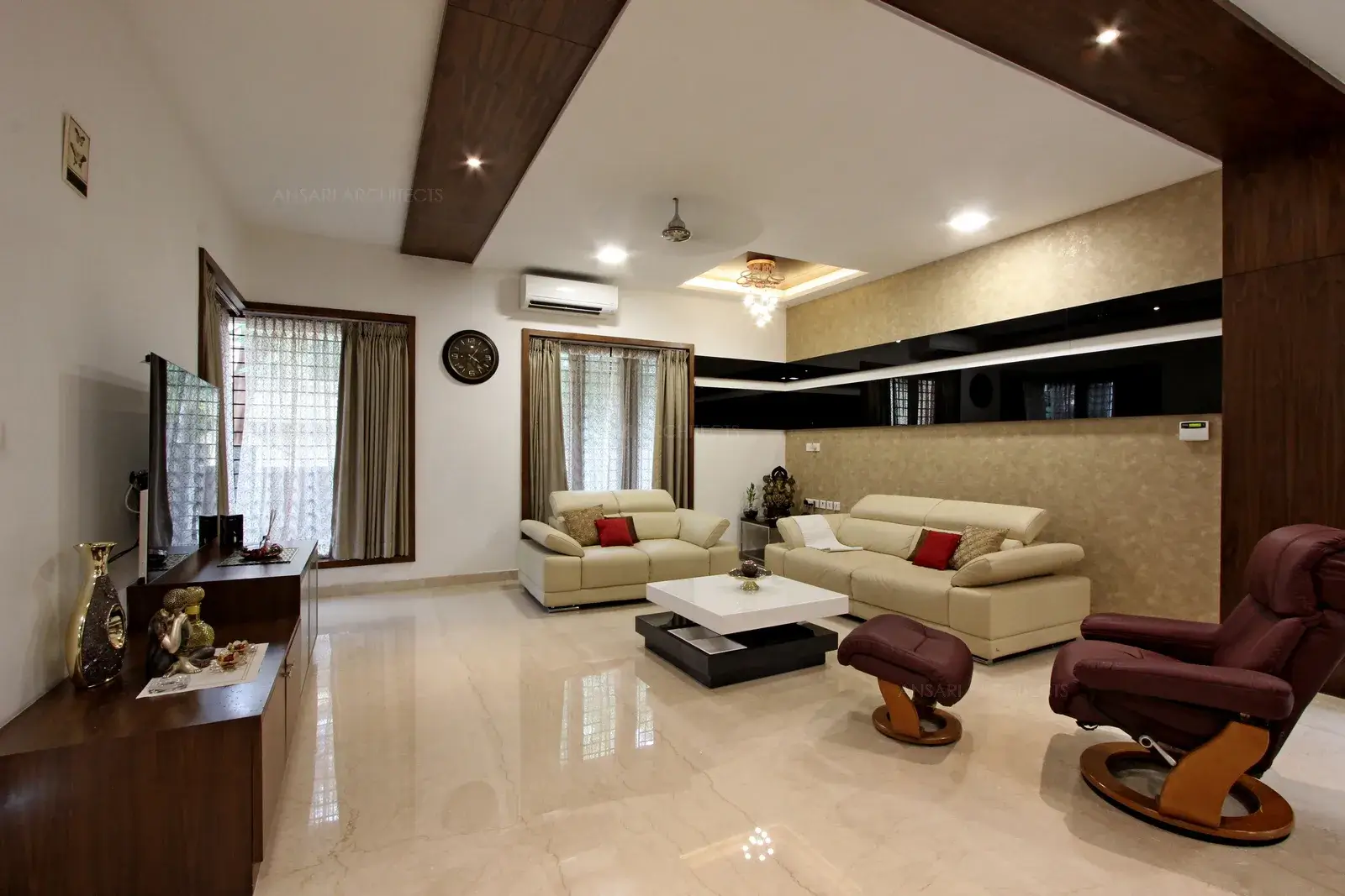 The spacious living space which further opens upto different spaces with the wallpaper and neutral lining along with the rich furniture. The veneer panelling through out the ceiling and floor complements the room with visual stimulation. The cosy furniture that meshes in style and colour with decor creating a contrast.