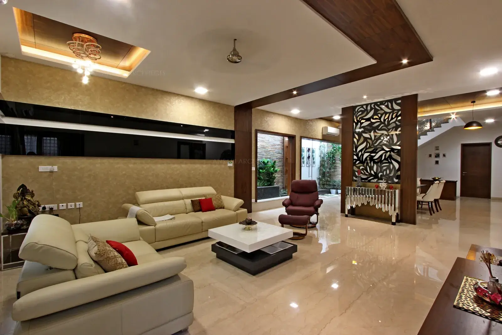 The recessed ceiling with veneer inset looks majestic with the decorative partition wall custom designed with glass cutout in leafy patterns. Free-standing frames on either sides with wood panelled textures looks antique connected with the dining area. A lone piece of ethnic furniture in a contemporary space lends local flavor to the space.