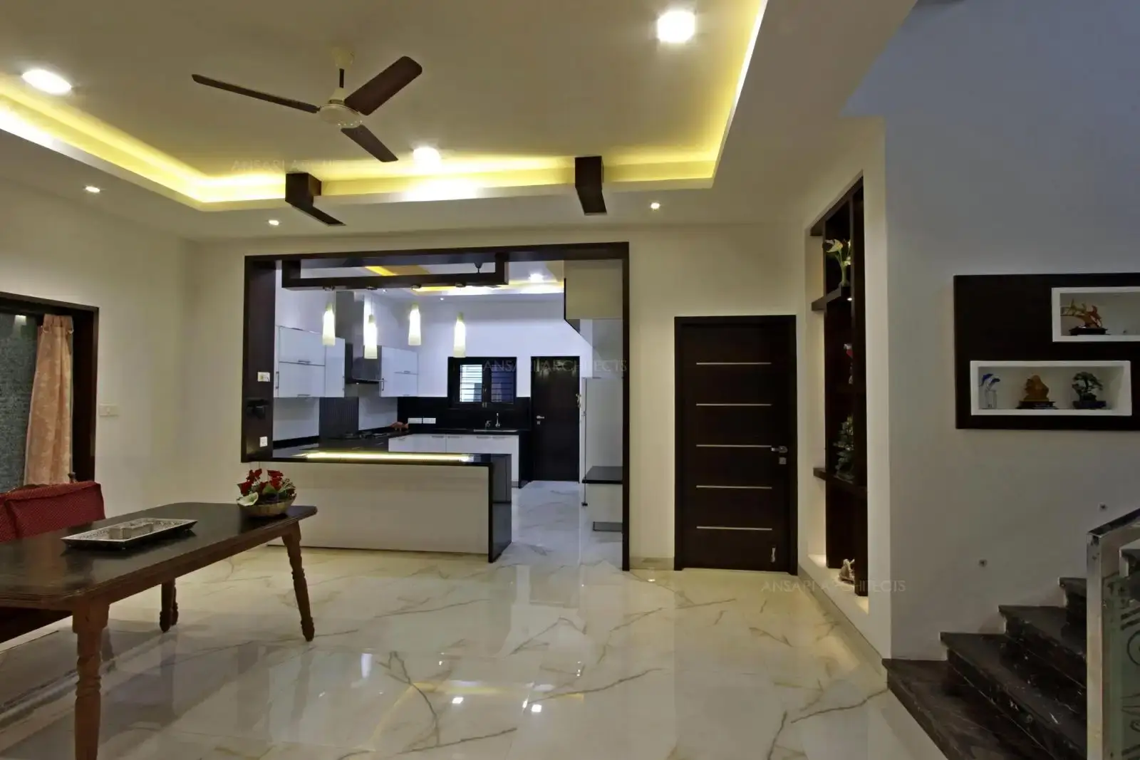 The kitchen is connected from the lobby area and the counter table acts as a partition demarcates the space along with the wooden panelling completes the touch of elegance here.