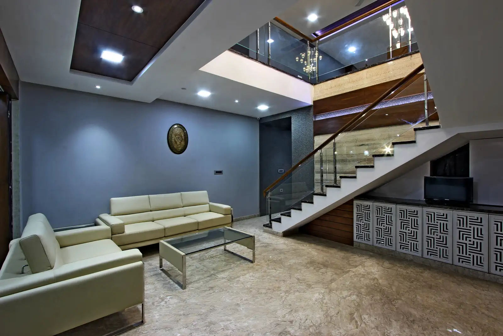 The sleek console is paired with veneer and recessed light creating a comfortable space. The space below the staircase is used for storage with patterns and complementing wood finishes provide degree of warmth.