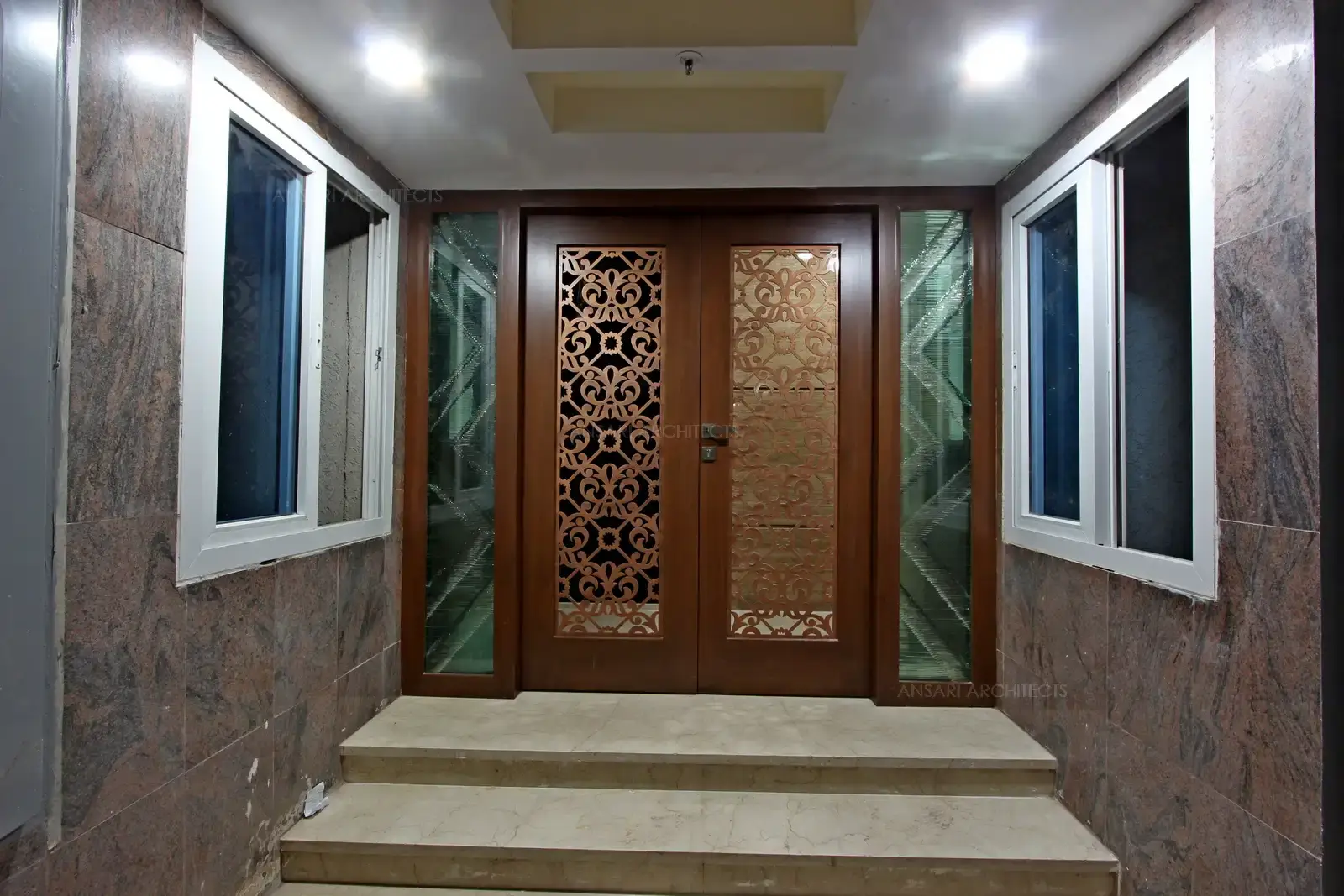 An antique door with floral grill patterns, opaque panel backdrop and glass work on either sides embellished for a warm welcome.