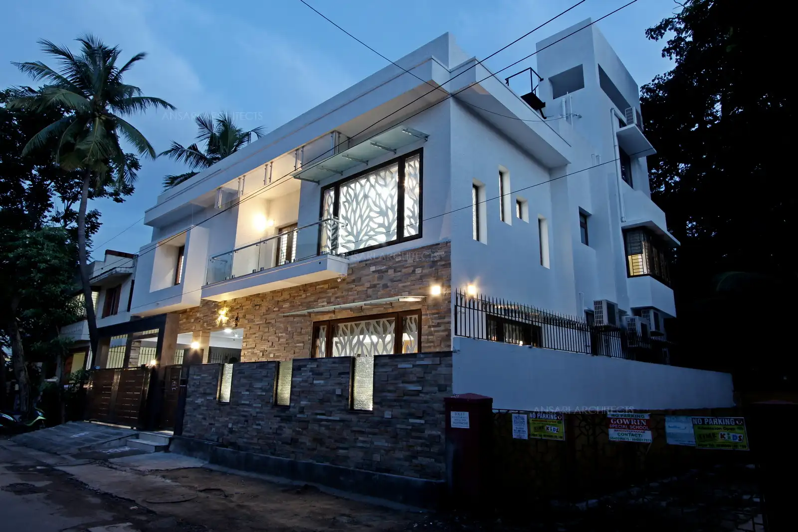 Muted exterior paint colour is juxtaposed with the lush, bright greenery. The contemporary exterior facade and the clean sructure give this home a open look. Stone along with white gives a welcoming look.